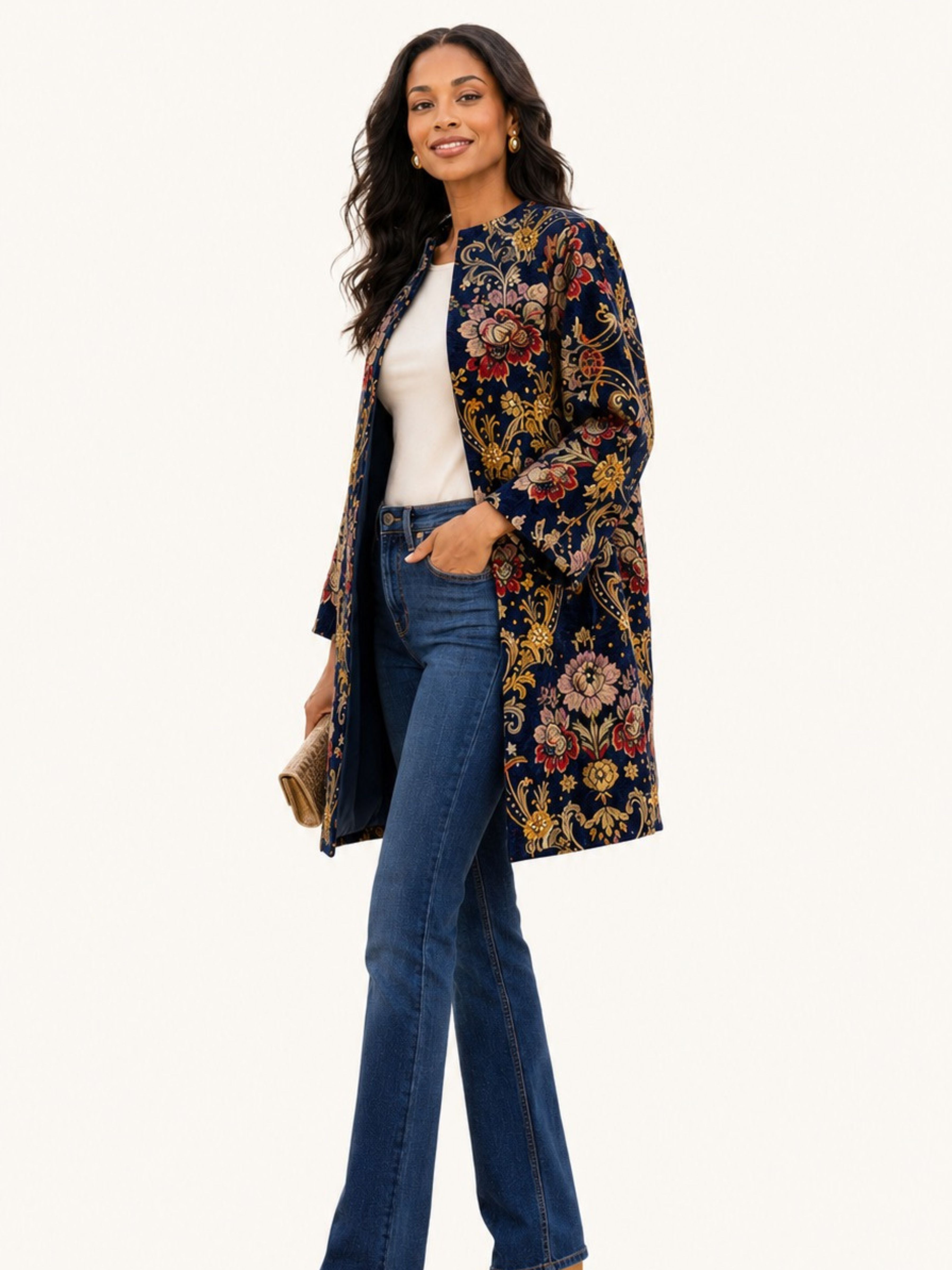 A woman modeling a navy blue open-front jacket with an intricate multicolor floral and paisley pattern, styled with a white top and blue jeans against a solid off-white background.