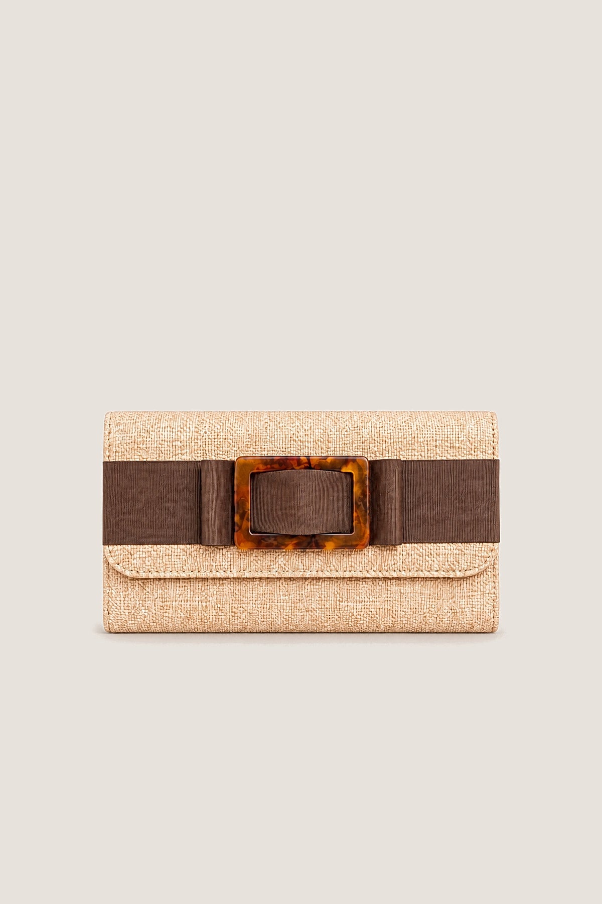 Avery clutch in natural straw with a chocolate brown flat bow and tortoise buckle, front view on a warm greige backdrop.