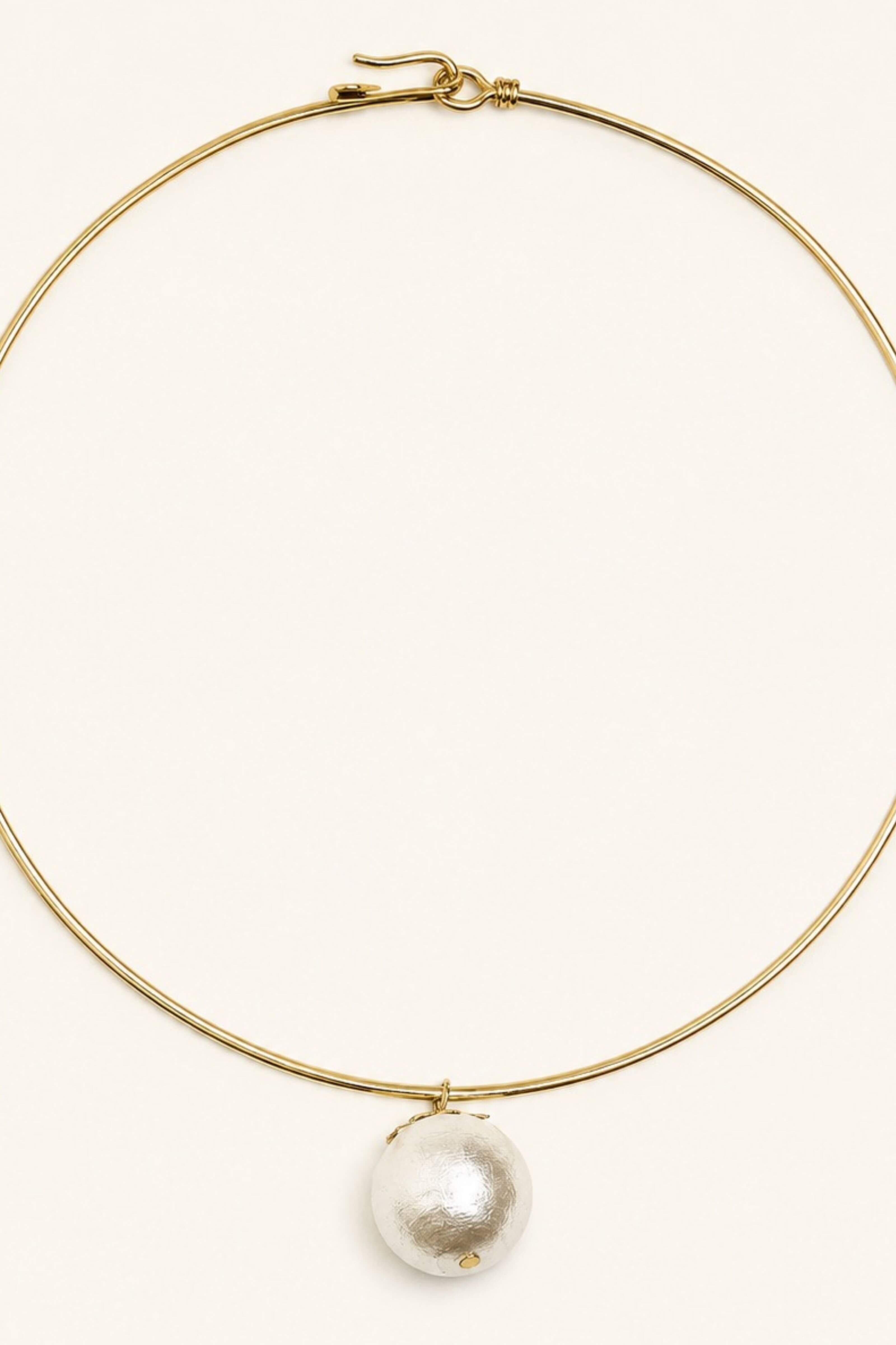 A delicate gold wire necklace with a single large, textured white pearl pendant, displayed on a clean, solid off-white background.