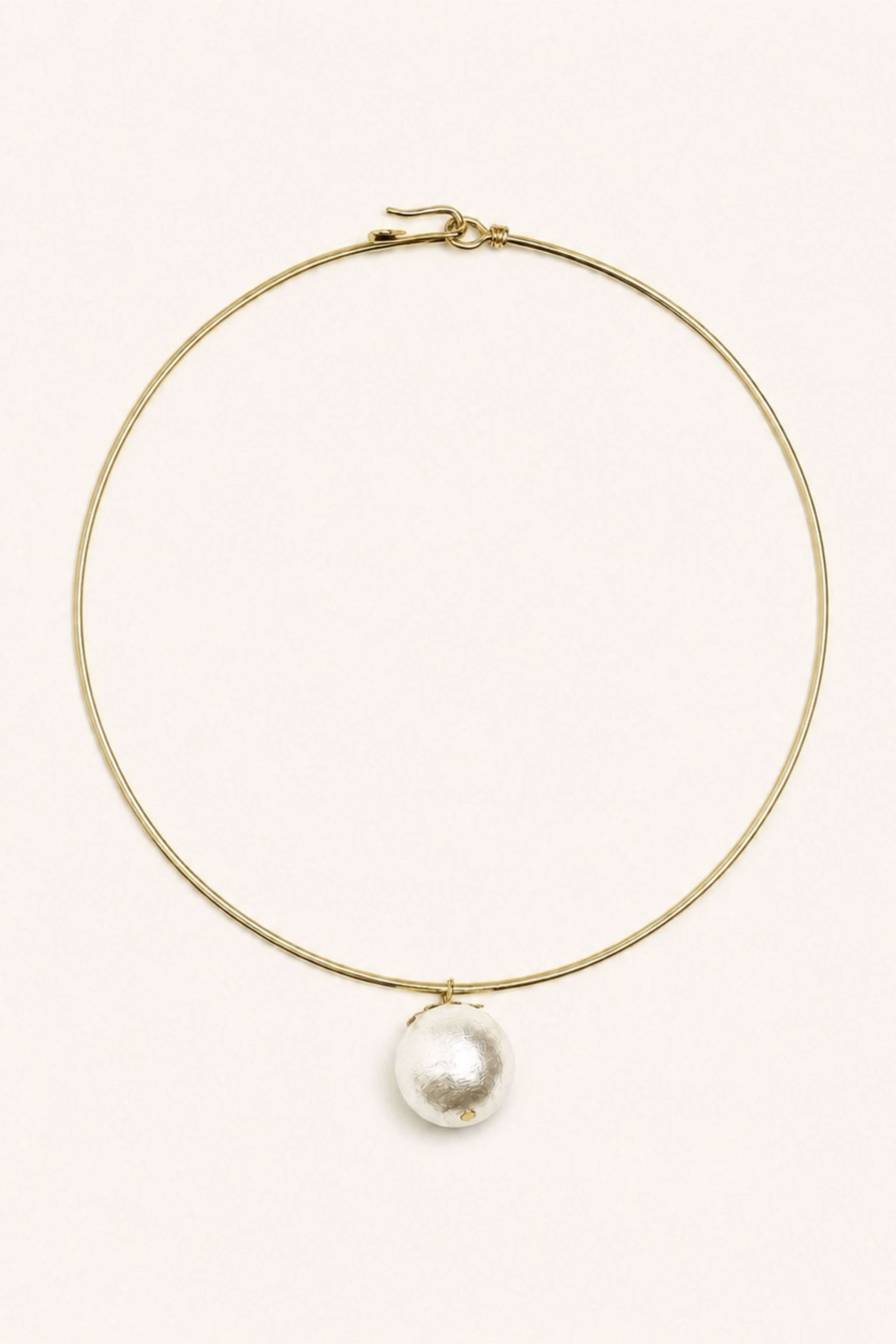 A delicate gold wire hoop necklace with a single large, irregular white pearl pendant, displayed on a clean, solid off-white background.