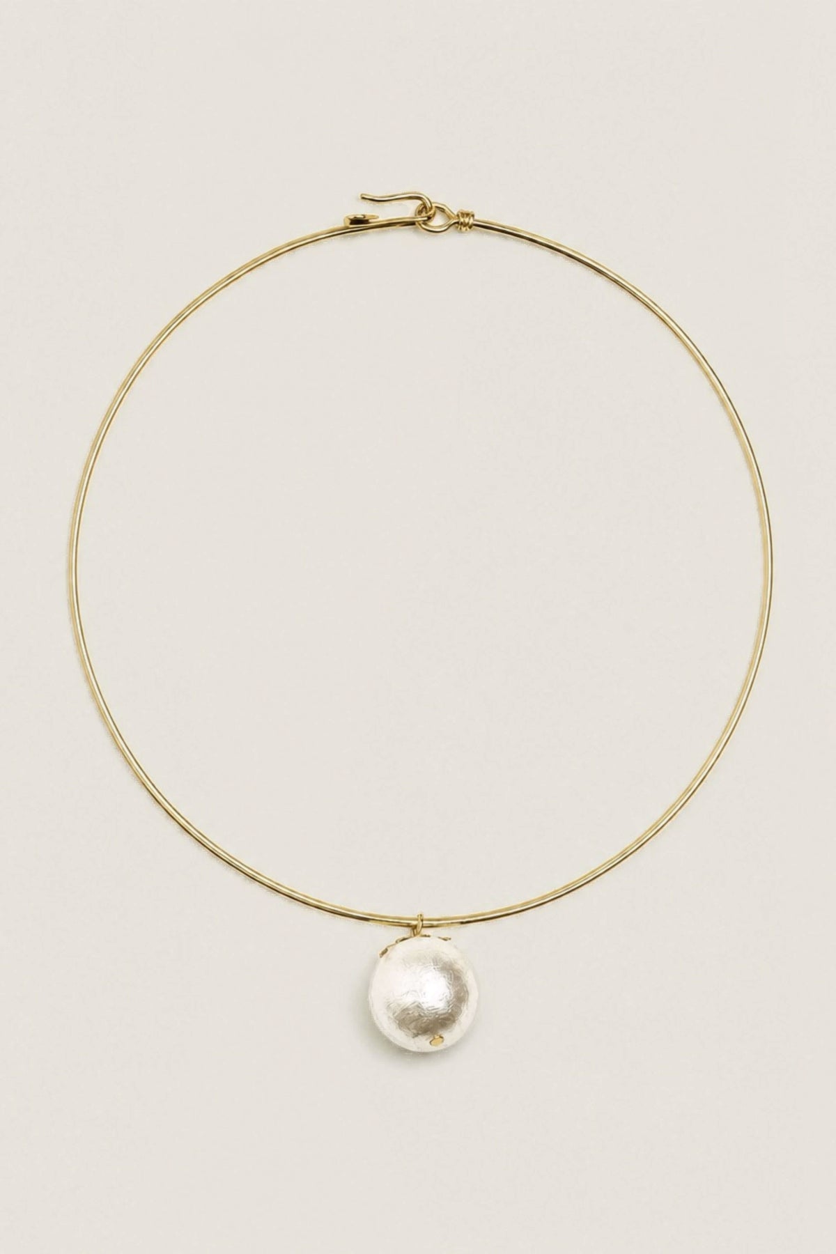 A delicate gold wire hoop necklace with a single large, irregular white pearl pendant, displayed on a clean, solid off-white background.
