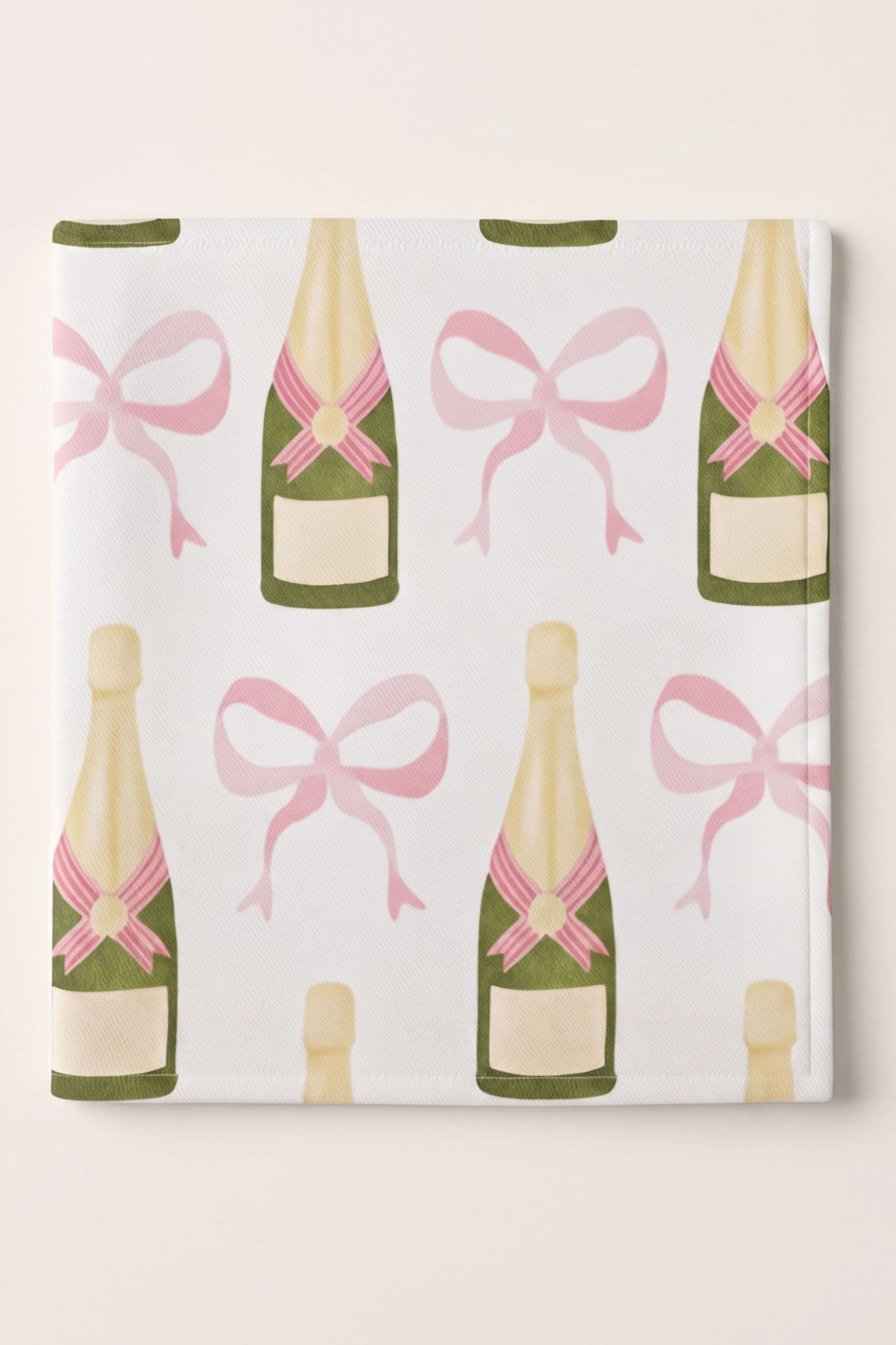 A square gift wrap or fabric sample featuring a repeating pattern of champagne bottles and pink bows on a white background, photographed against a light beige backdrop.