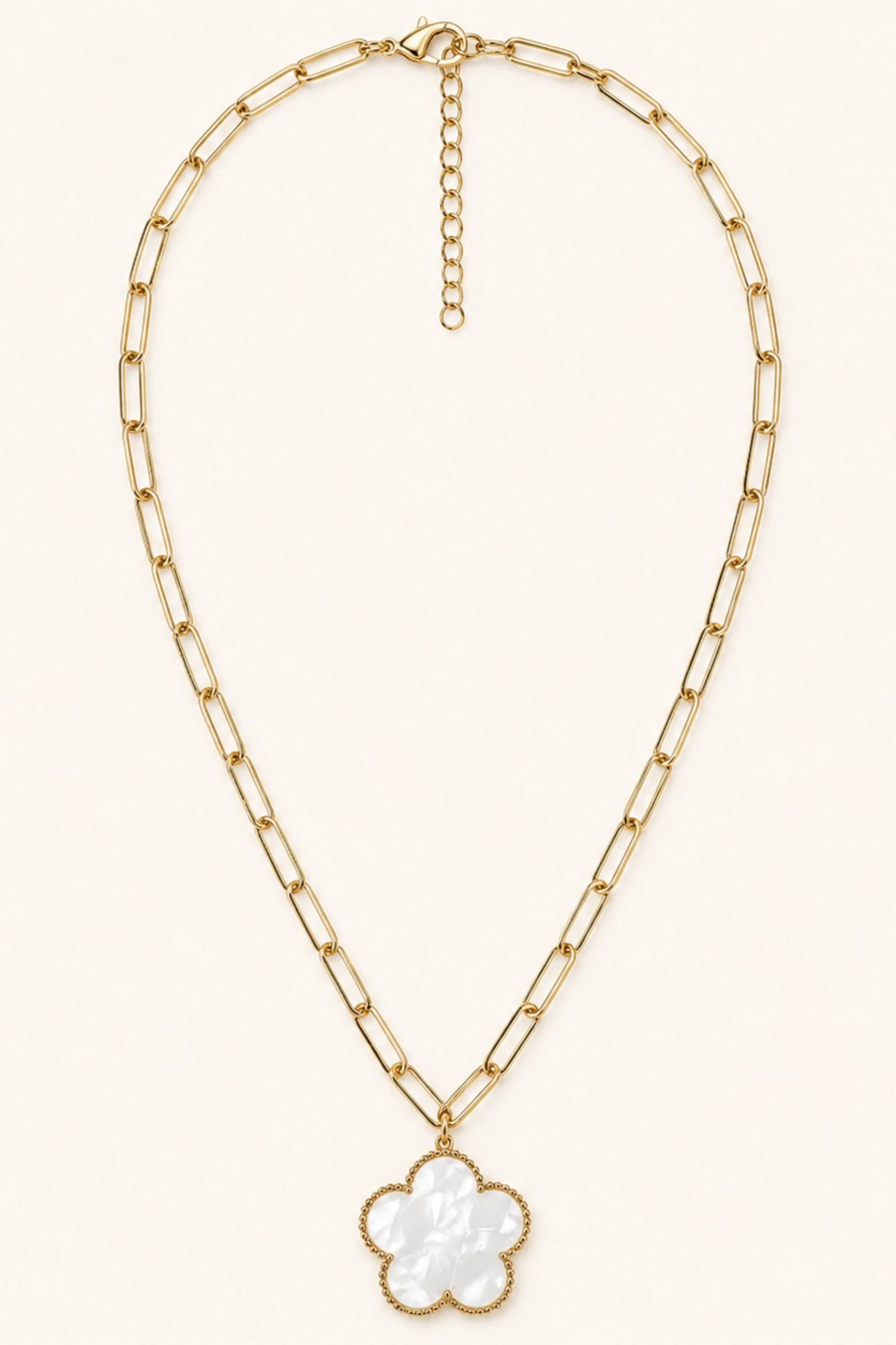 A gold paperclip chain necklace with a white mother-of-pearl clover pendant, displayed on a clean off-white background.
