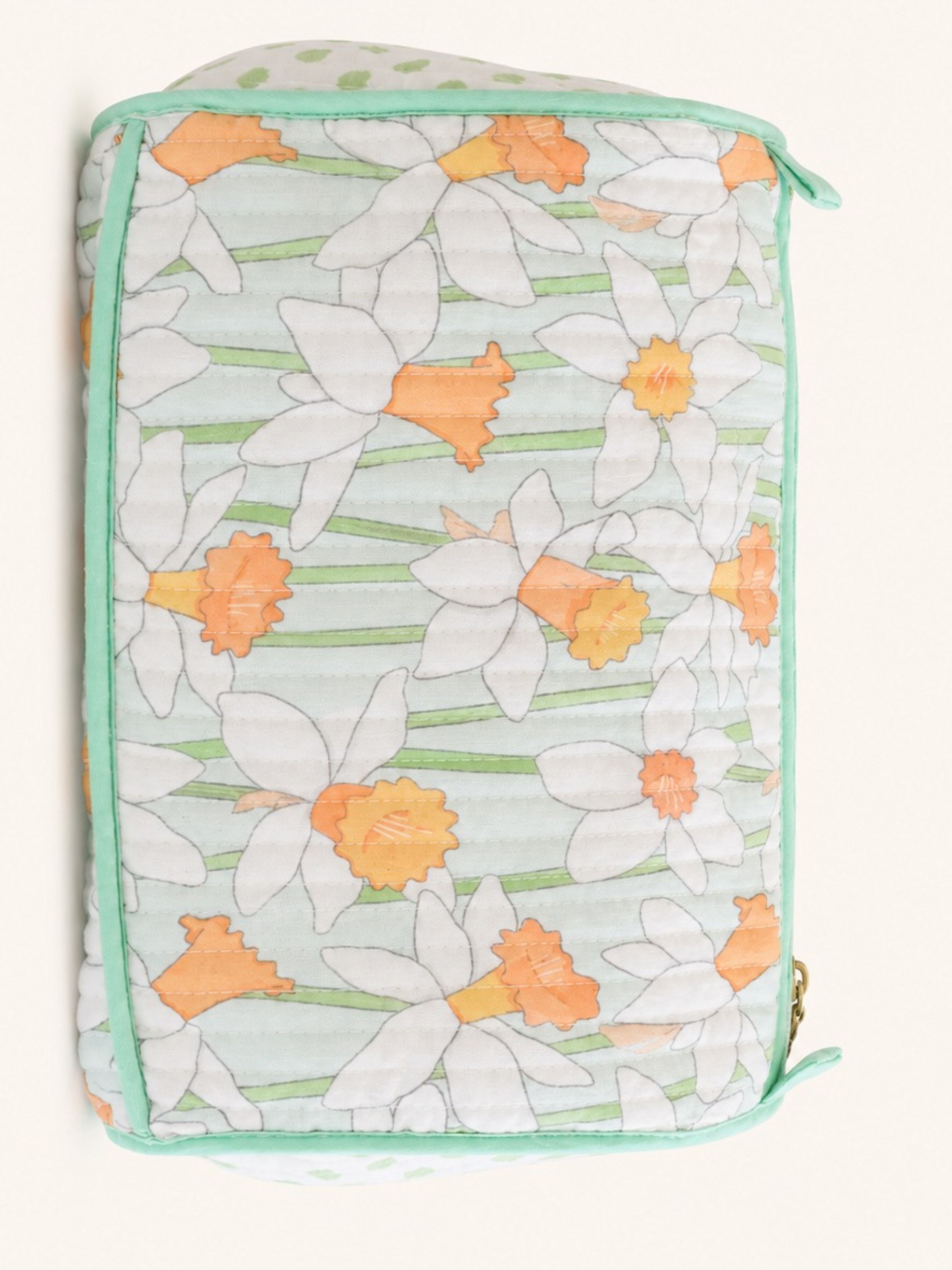 A quilted fabric pouch featuring a daffodil pattern in white, orange, and light green, with mint green piping and a zipper closure.