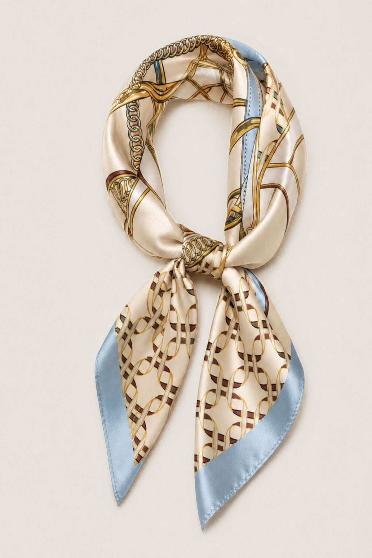 A silk scarf with a beige and gold geometric chain-link pattern and light blue edges, tied in a loop on a light cream background.
