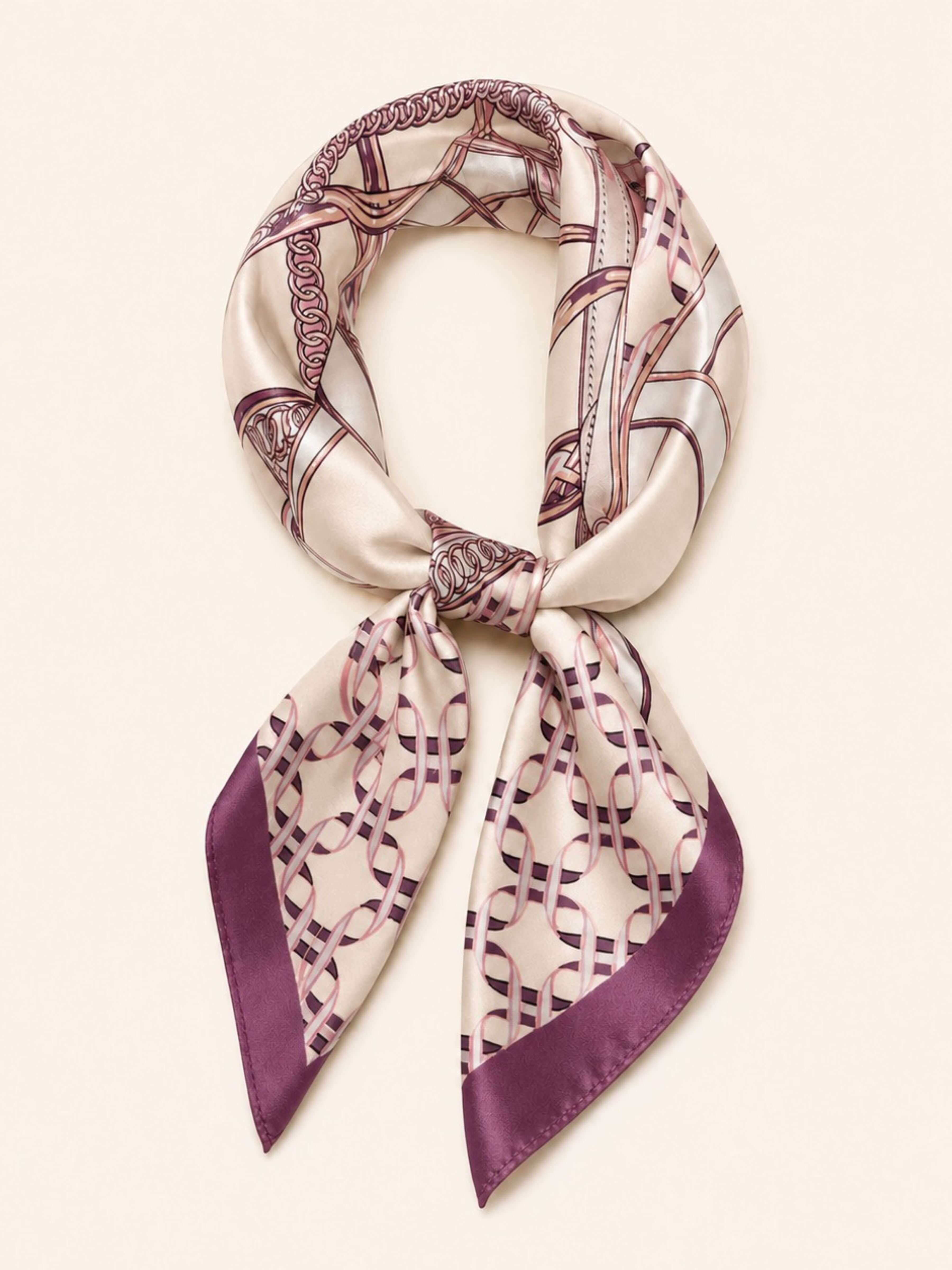 A silk scarf with a geometric interlocking chain pattern in purple and beige, tied in a knot and displayed against a light cream background.