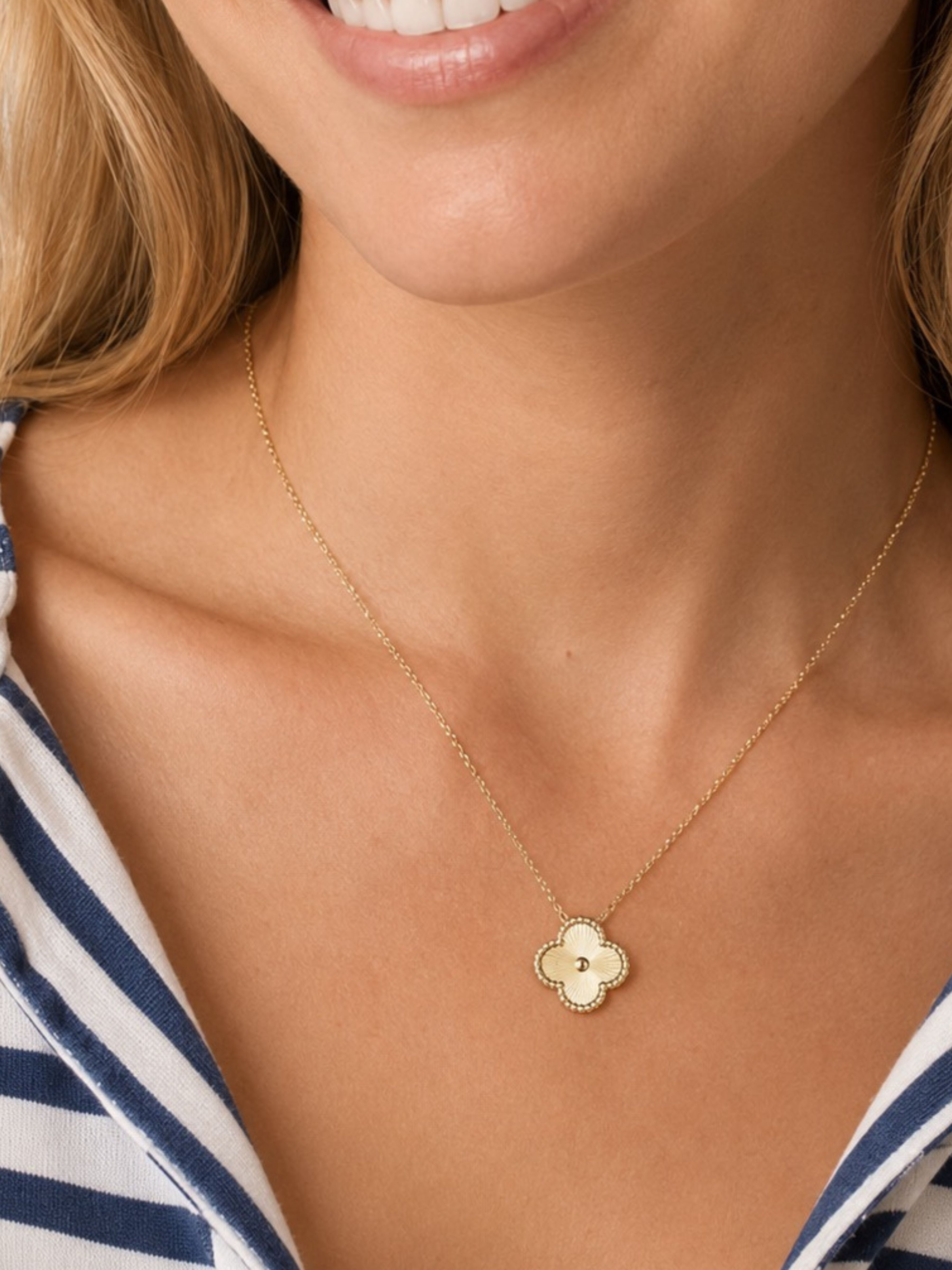 A close-up of a woman wearing a delicate gold chain necklace with a small clover-shaped pendant featuring a white center.