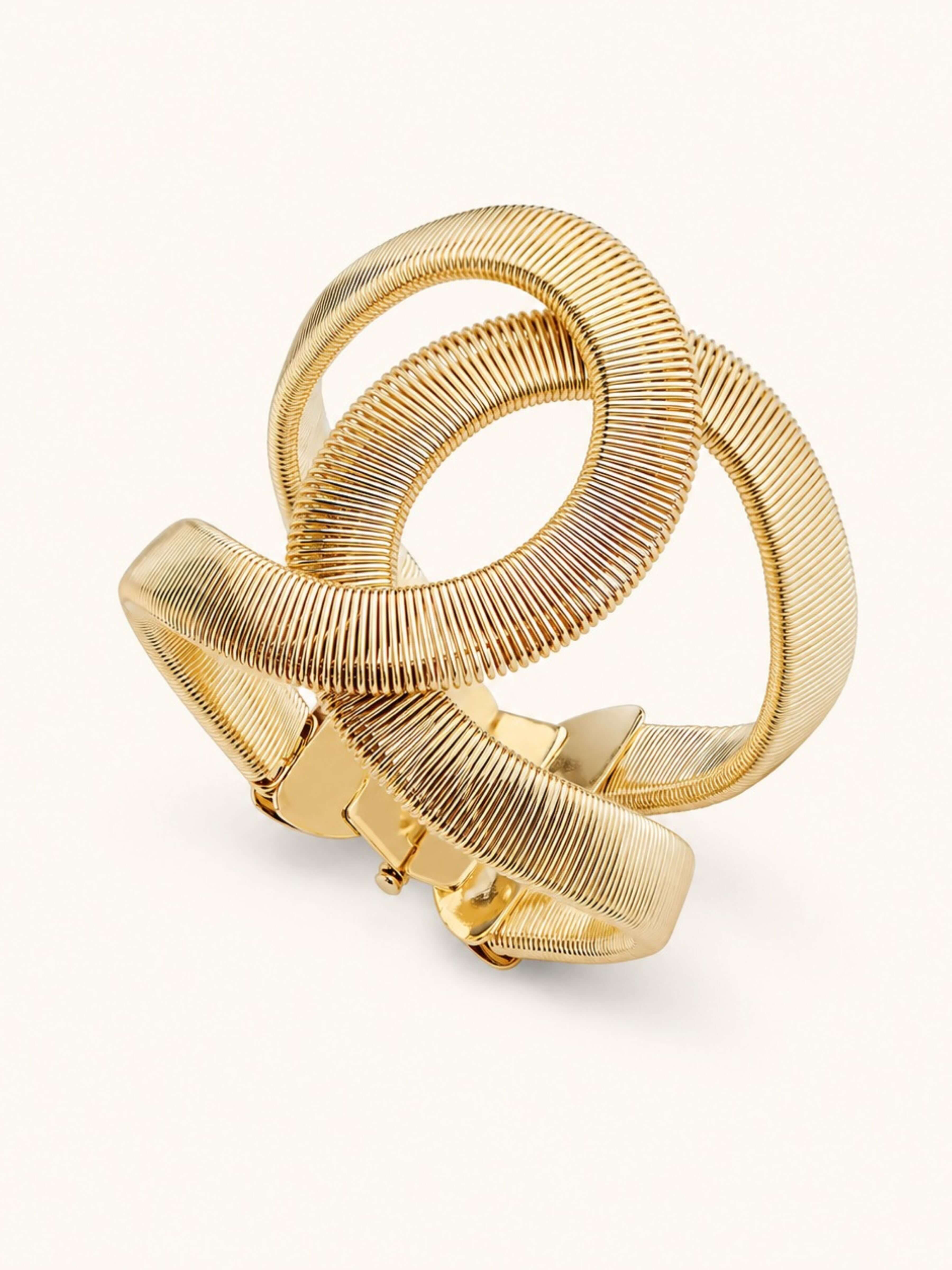 A chunky gold-toned metal cuff bracelet with a textured, ribbed snake-skin style design and a sliding clasp, shown on a clean off-white background.