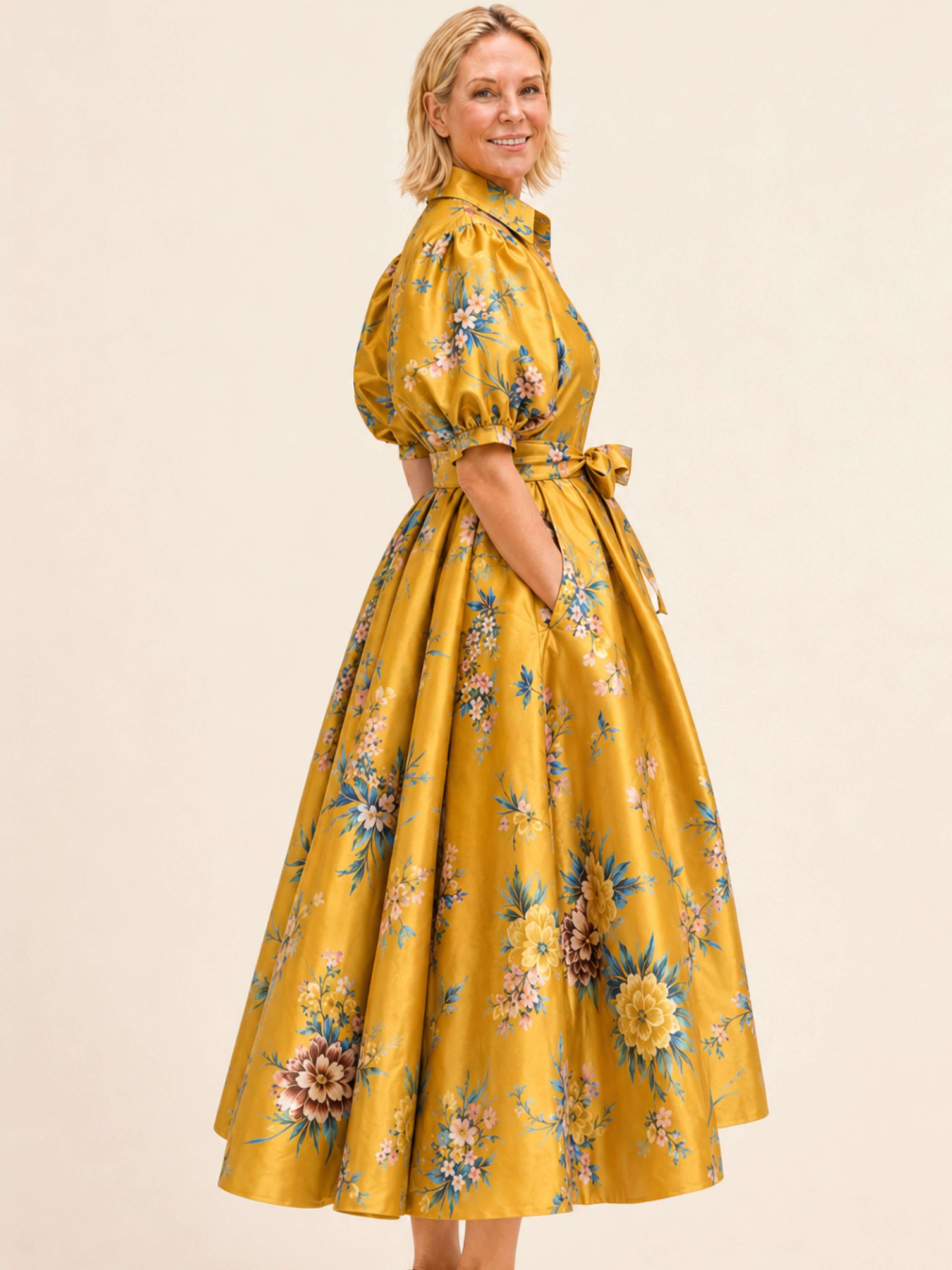 A woman modeling a yellow midi dress with a floral print, featuring puff sleeves and a matching waist tie, set against a plain beige background.