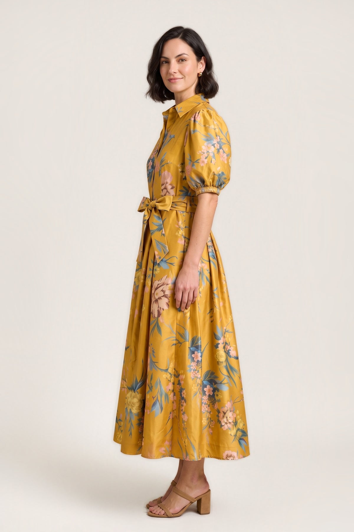 Side view of the Golden Garden puff sleeve maxi dress, showing the puff sleeve, the bow at the waist and the full skirt, on a warm neutral studio background.