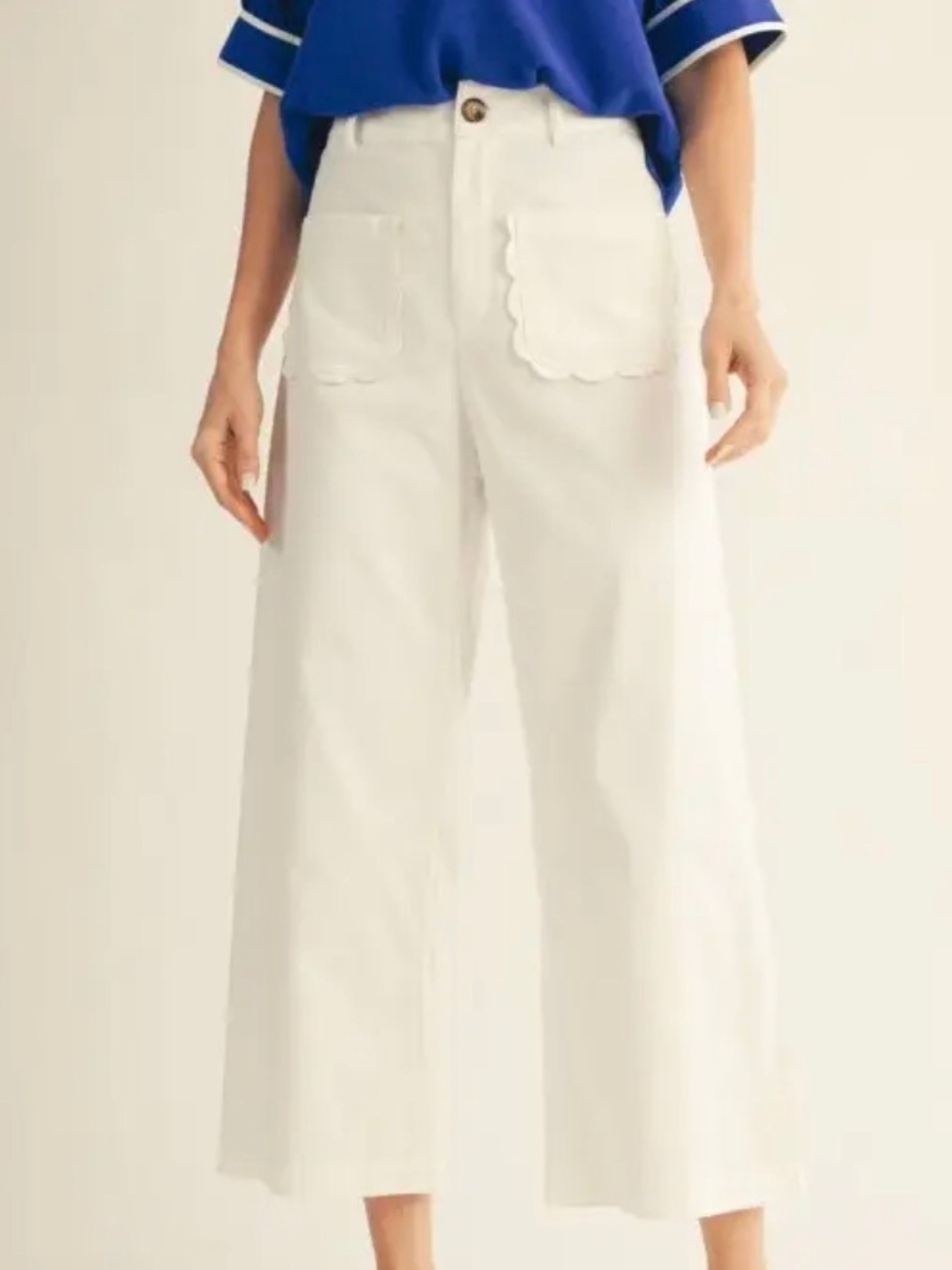 White cropped wide-leg pants with scalloped pocket edges, shown on a model wearing a blue top against a plain light background.