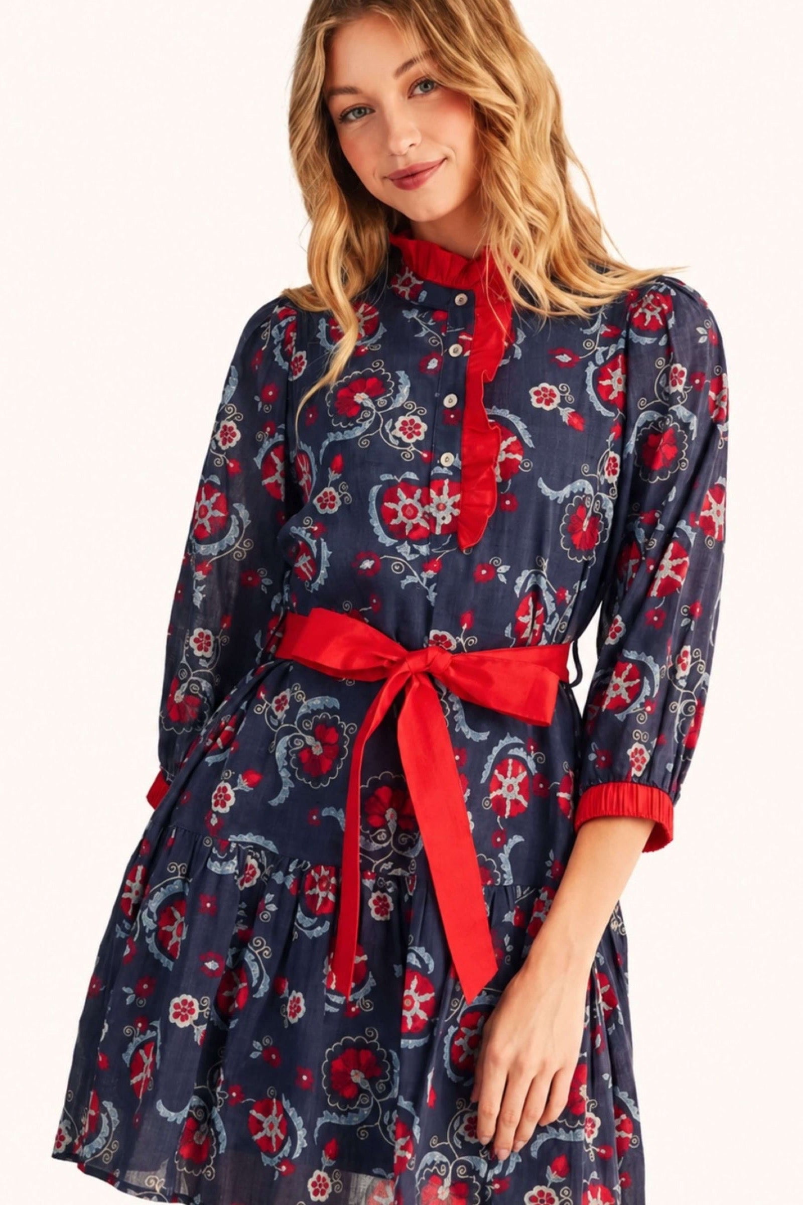 A woman wearing a navy blue midi dress with a red and white floral pattern, featuring a red tie-neck bow and a matching red waist tie belt.