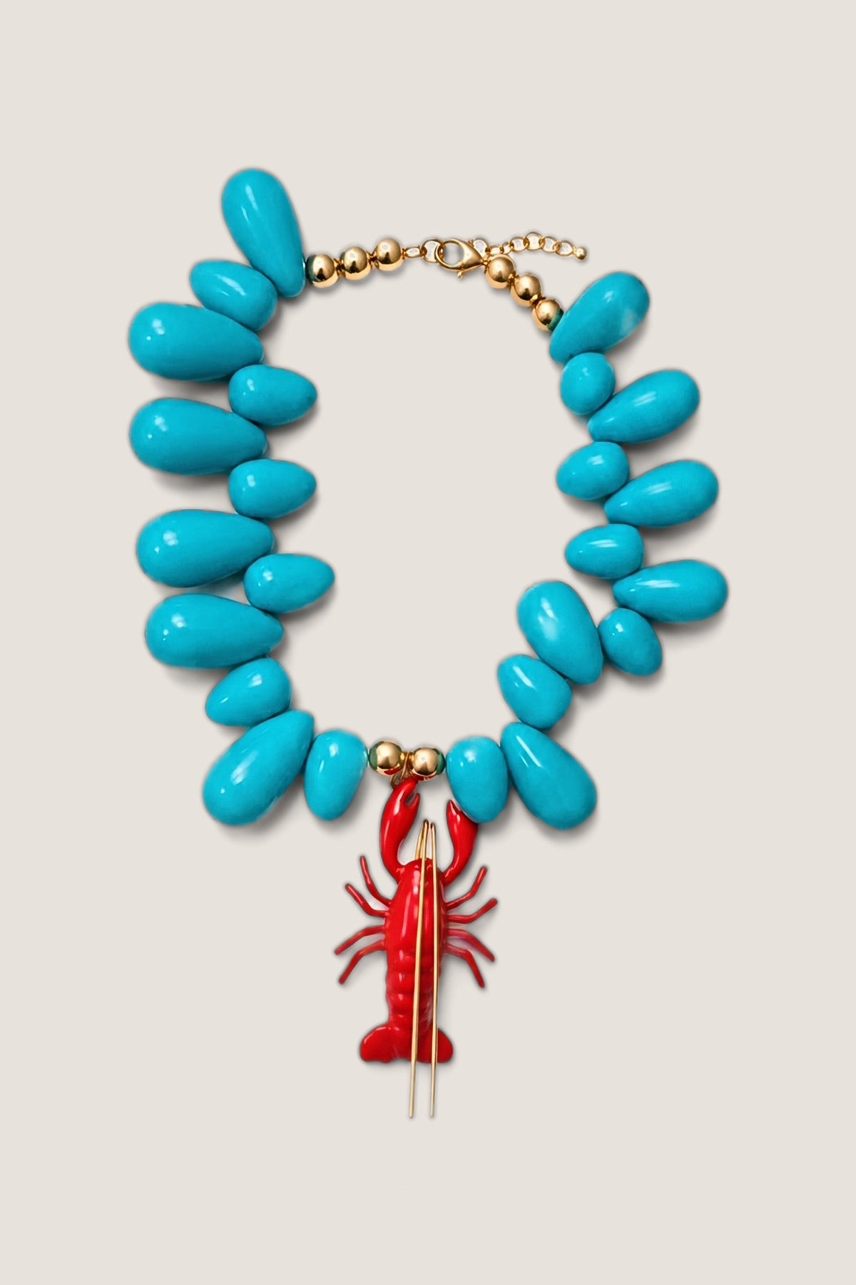 Lobster Kitsch and Sea necklace laid flat: sky blue teardrop resin beads with gold bead accents and a red enamel lobster pendant