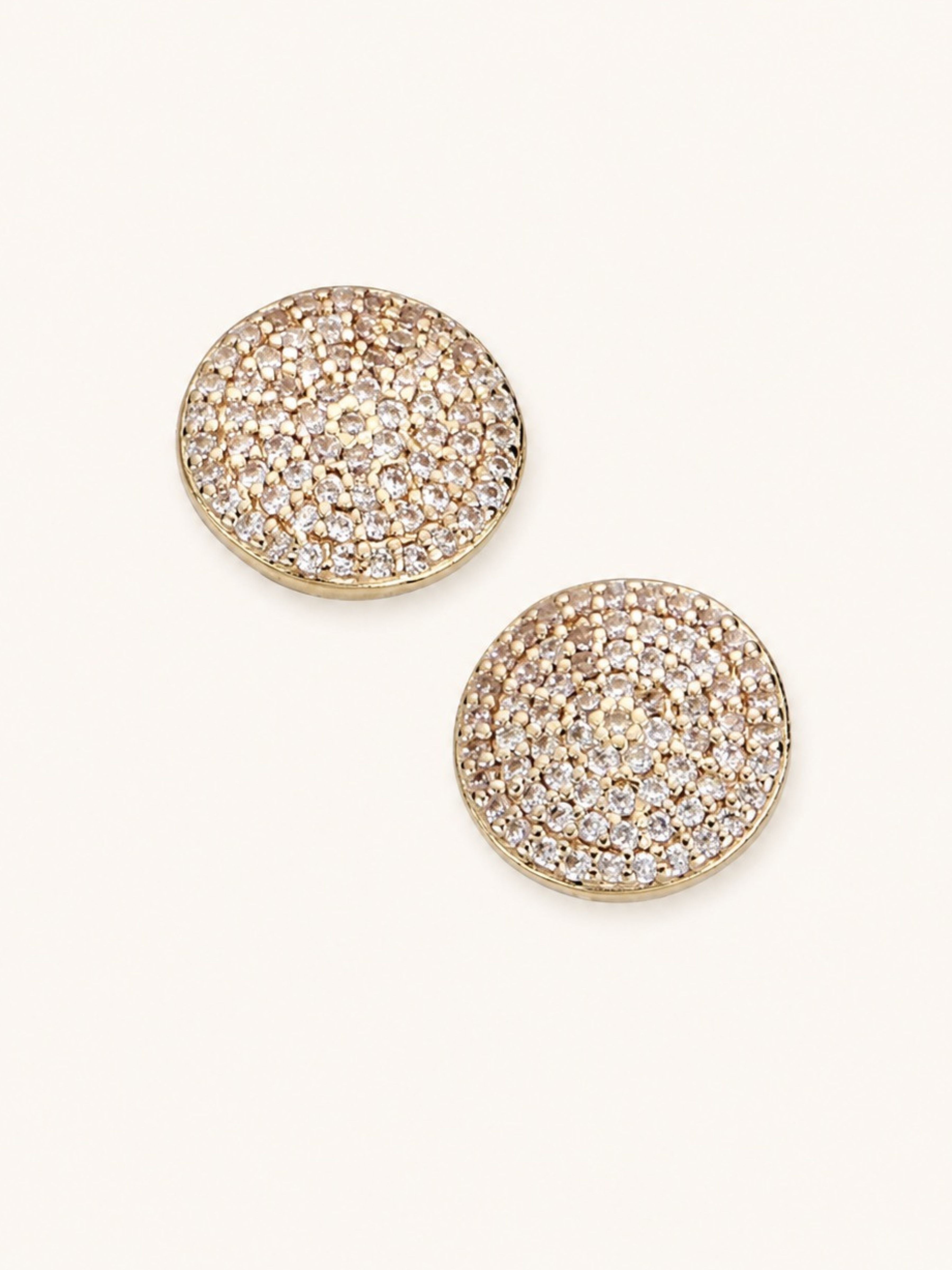A pair of round gold-tone stud earrings covered in small clear pavé stones, displayed on a light cream background.