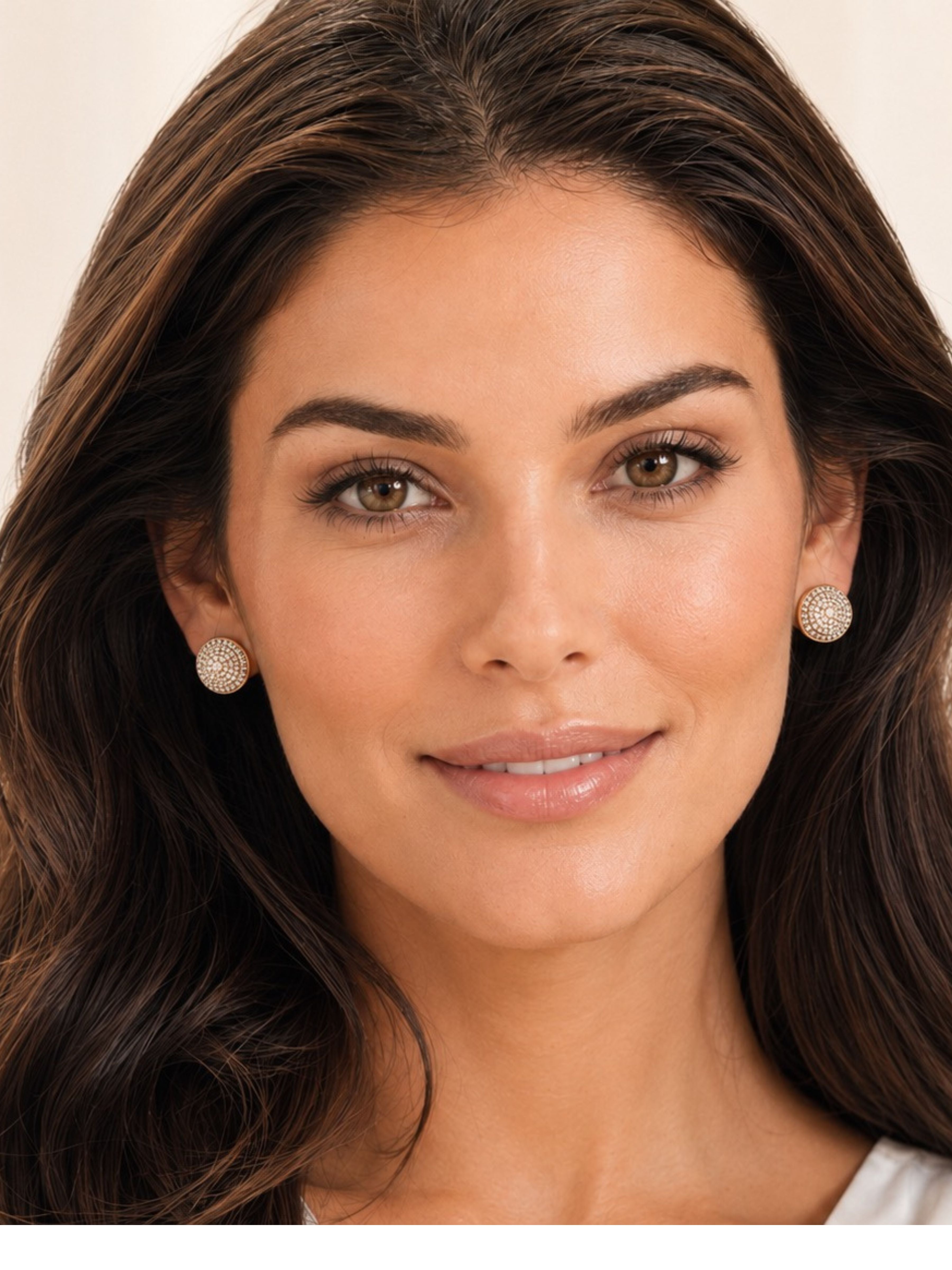 A close-up portrait of a woman with long dark brown hair wearing textured gold-toned stud earrings against a soft beige background.
