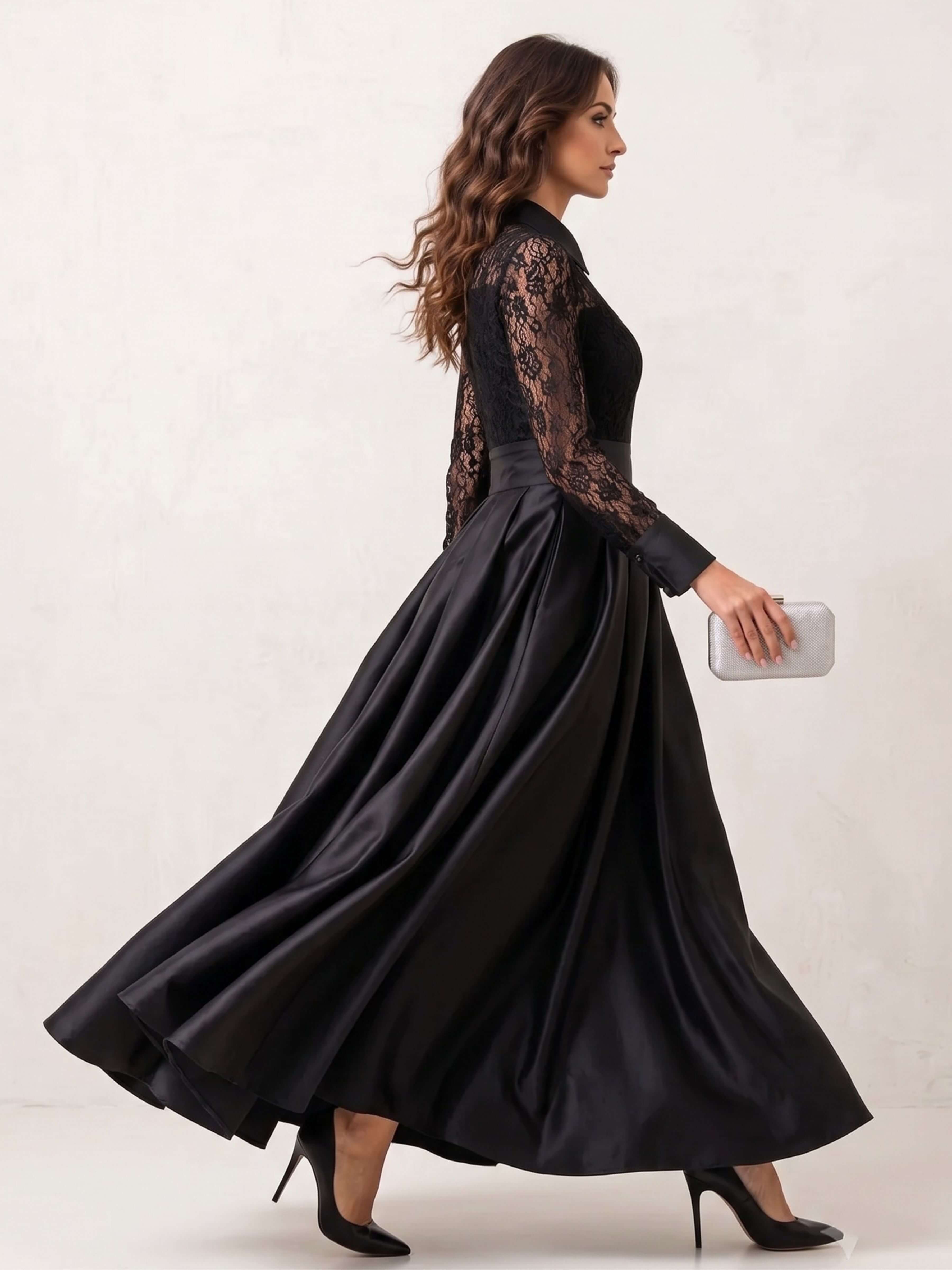 A woman modeling a long black satin maxi dress with sheer black lace sleeves and a lace bodice, shown from the side against a light beige studio background.