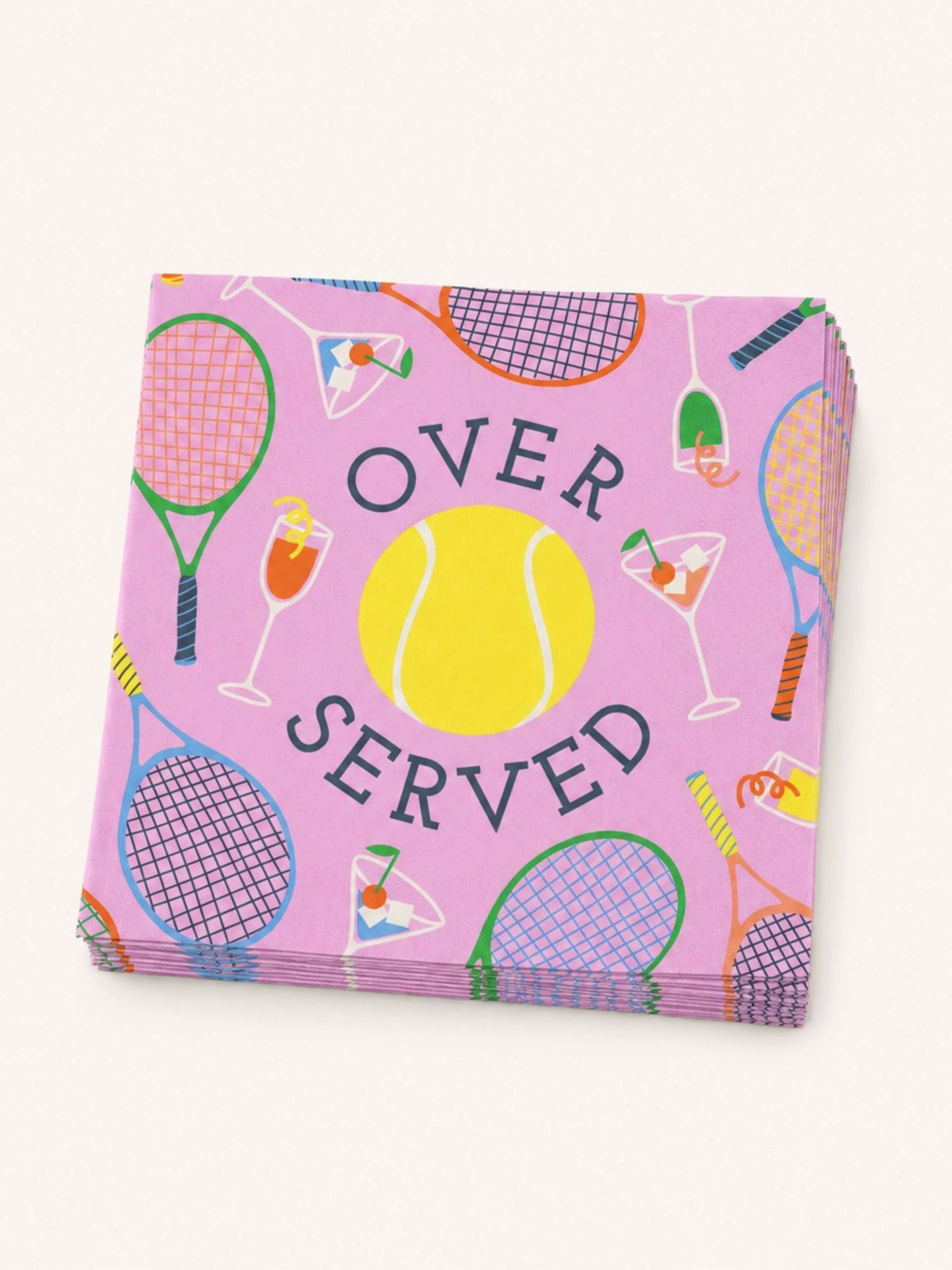 A stack of pink paper napkins featuring a tennis-themed pattern with rackets, a yellow tennis ball, cocktail glasses, and the words 'OVER SERVED' in dark lettering, shown on a light beige background.