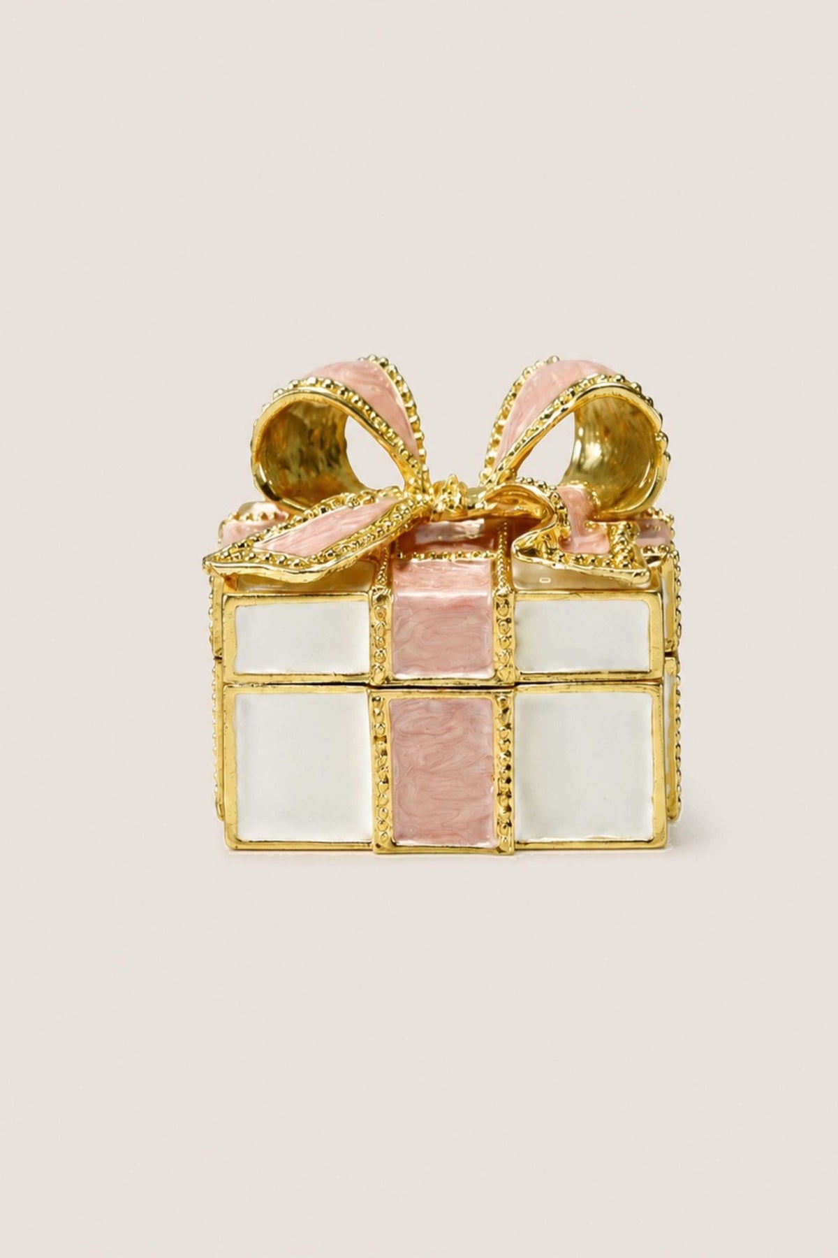 A gold-plated gift box ring with pink enamel panels and a pink ribbon bow, set against a plain off-white background.