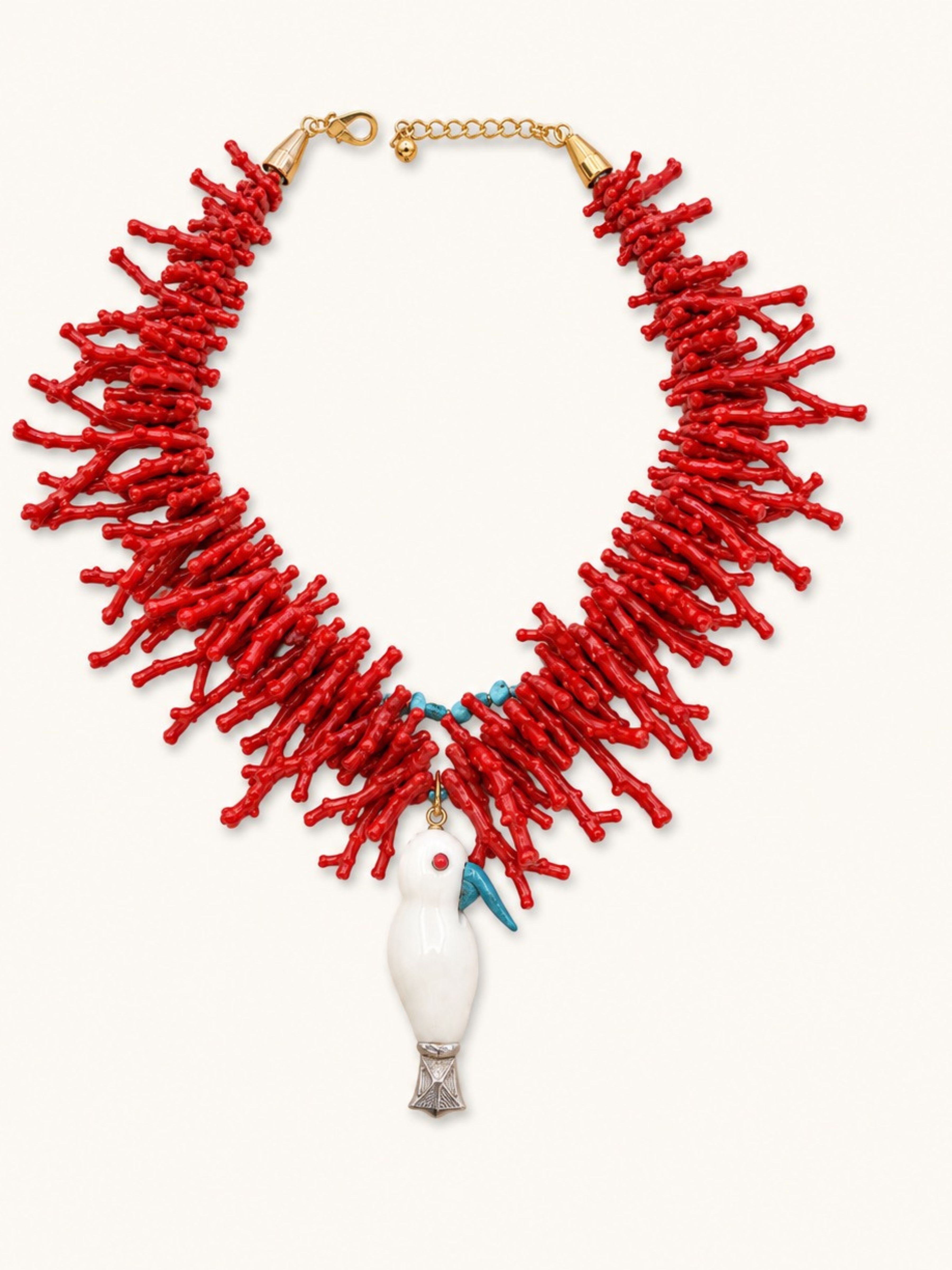 A statement necklace featuring a dense collar of bright red coral-like strands, a gold-tone chain extender and clasp, a white dove pendant, and small turquoise and red details.