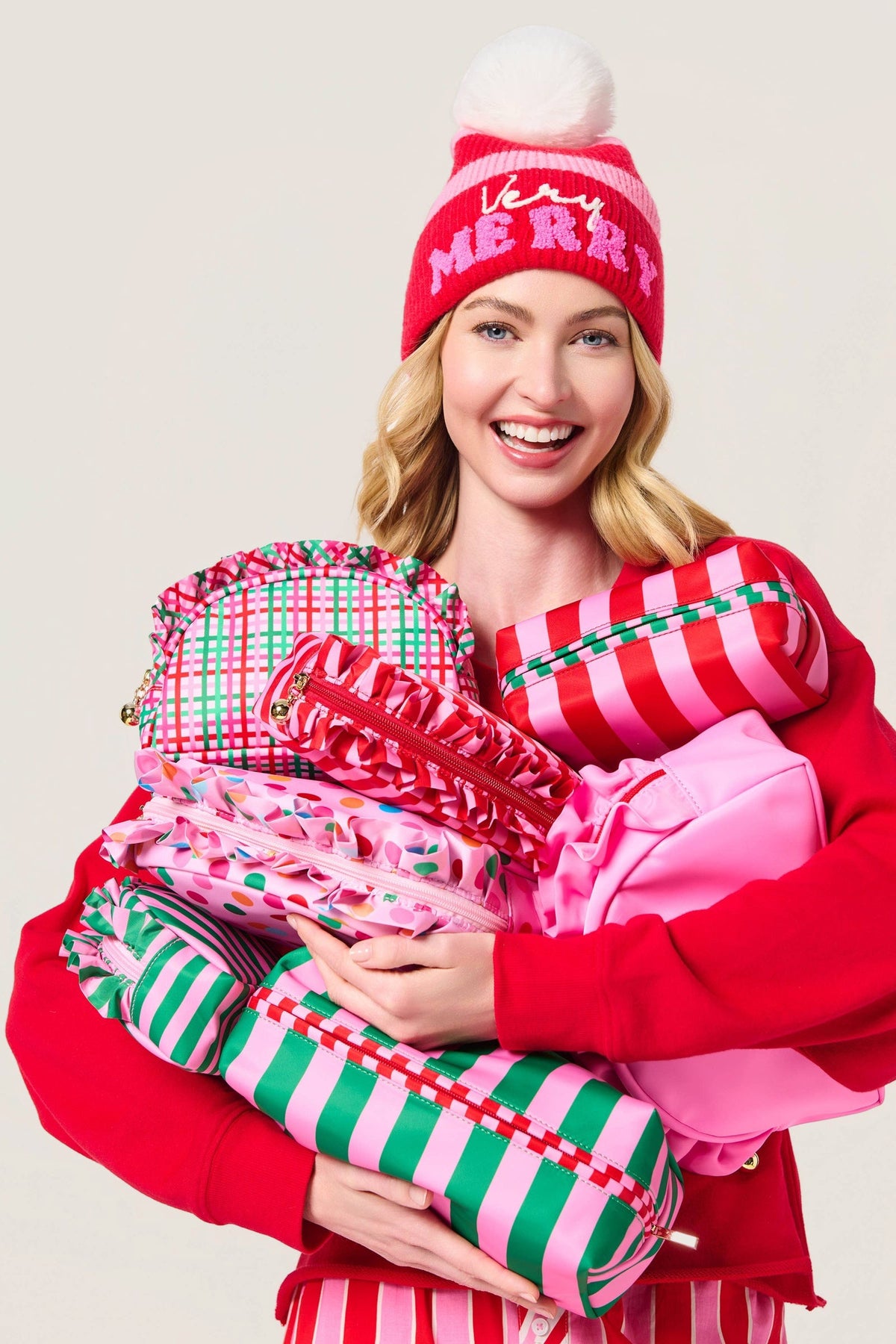 Woman in a red sweater and holiday beanie holding a stack of zip pouches, the Small Plaid Ruffle Zip Pouch at the top left