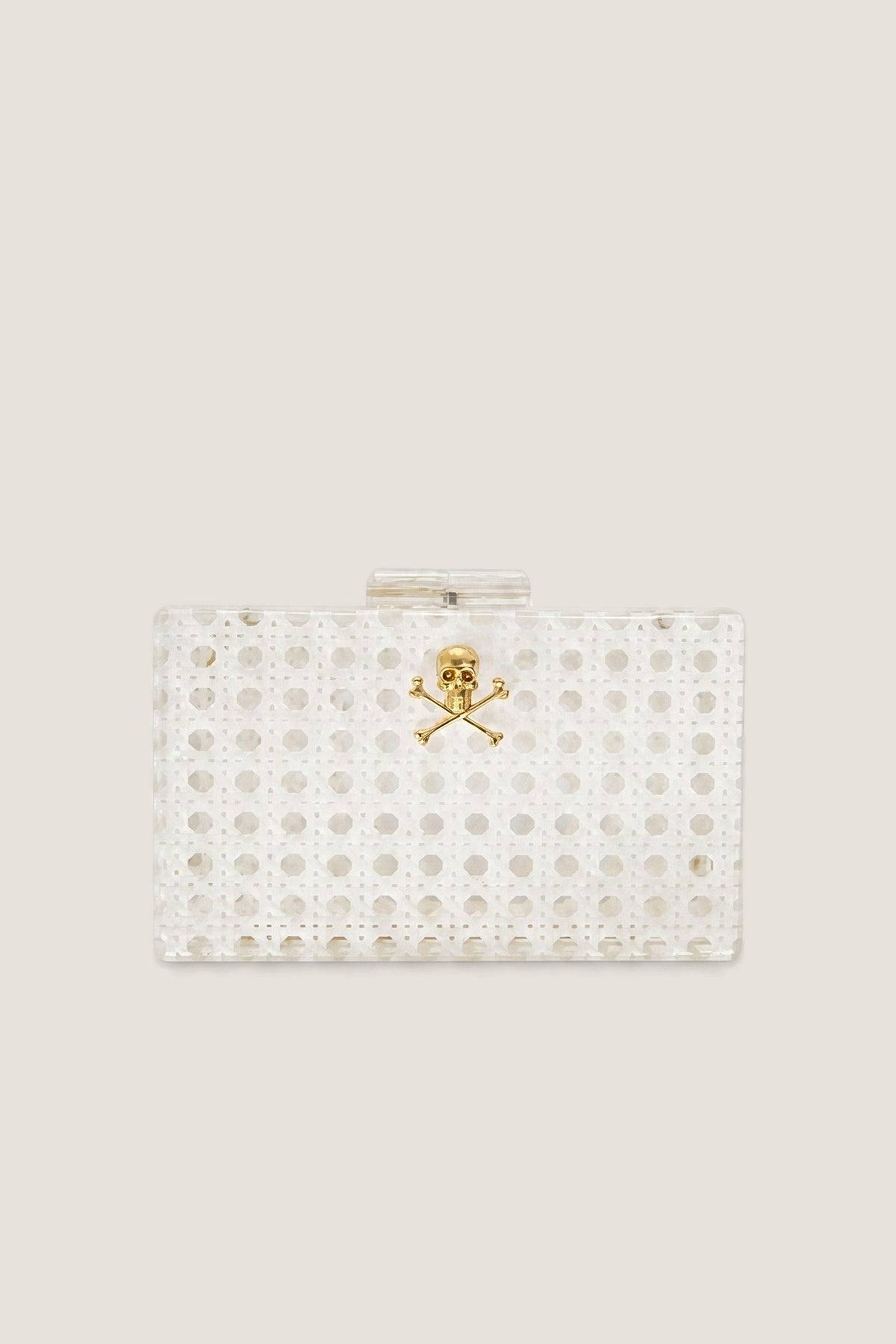 The White Breakers Clutch, a white caned acrylic minaudière with a gold skull and crossbones on the front, shown front on.