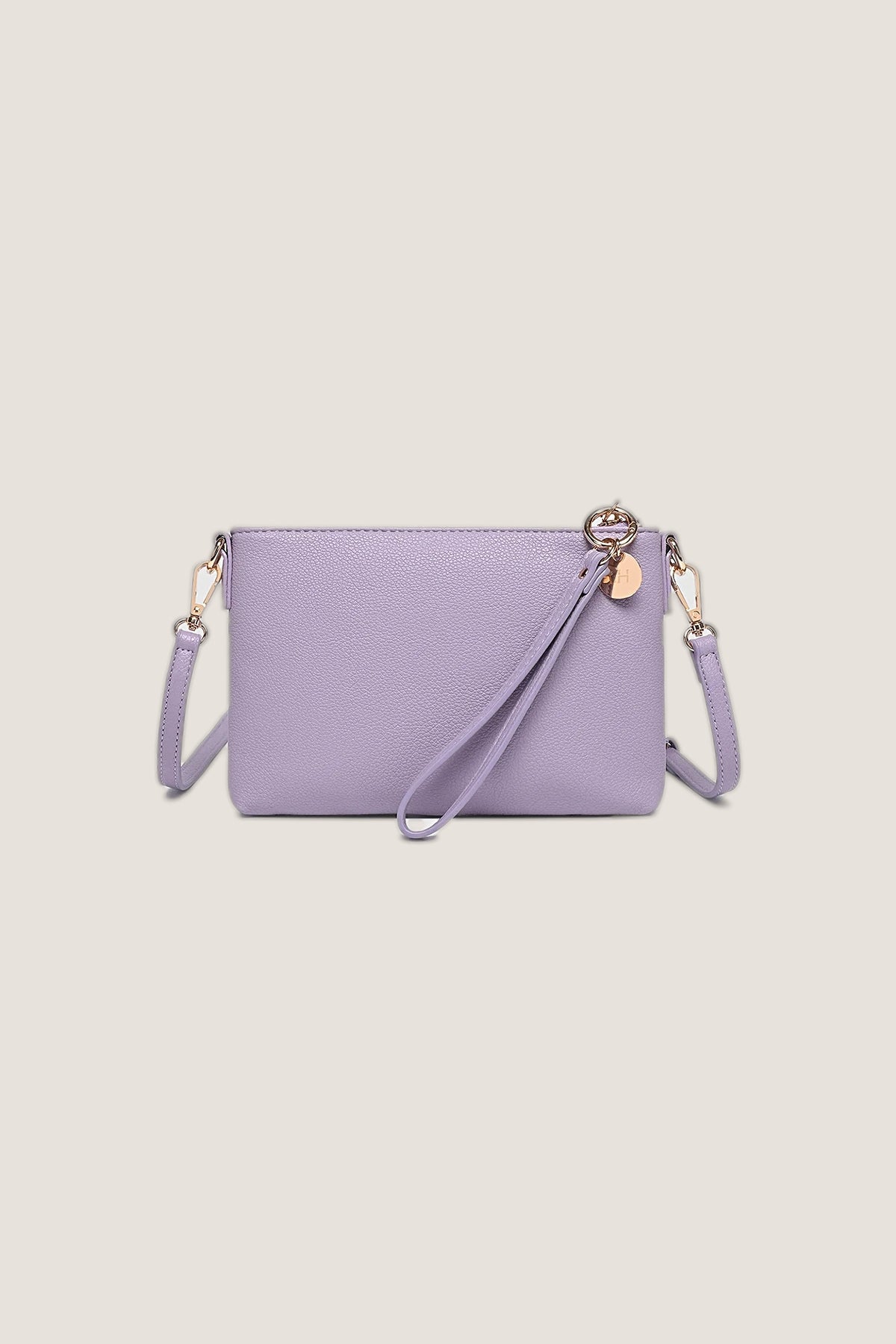 Baby Sophie Lilac Crossbody Bag in smooth lilac vegan leather with a wristlet strap, rose gold charm and light gold hardware, front view on a warm greige backdrop.