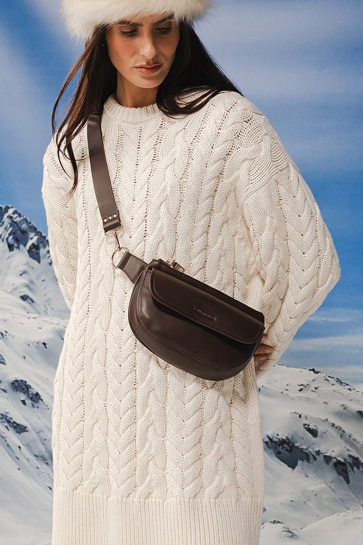 The Lola Chocolate Belt Bag worn across the body at the hip with a long cream cable knit sweater dress.