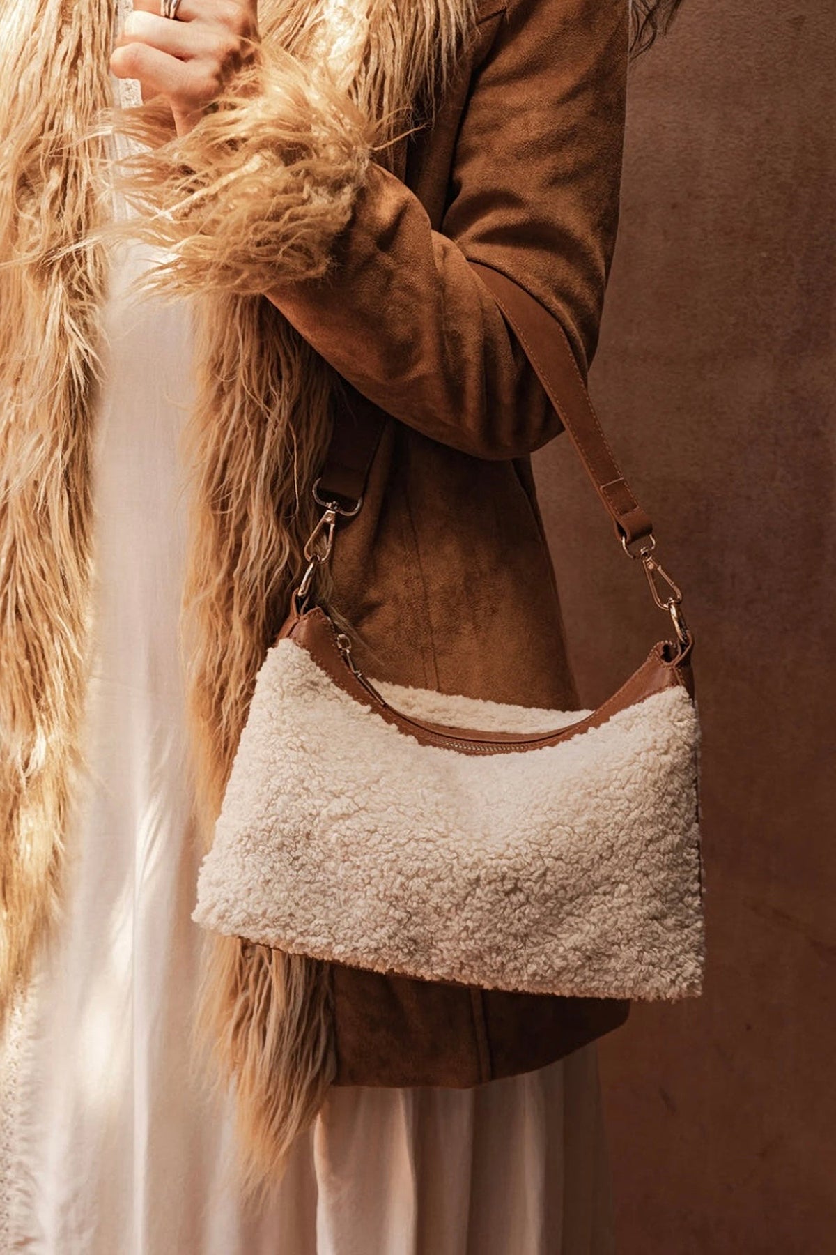 The Beige Aspen Shoulder Bag worn on the shoulder with a suede jacket, a faux fur vest and a cream dress.