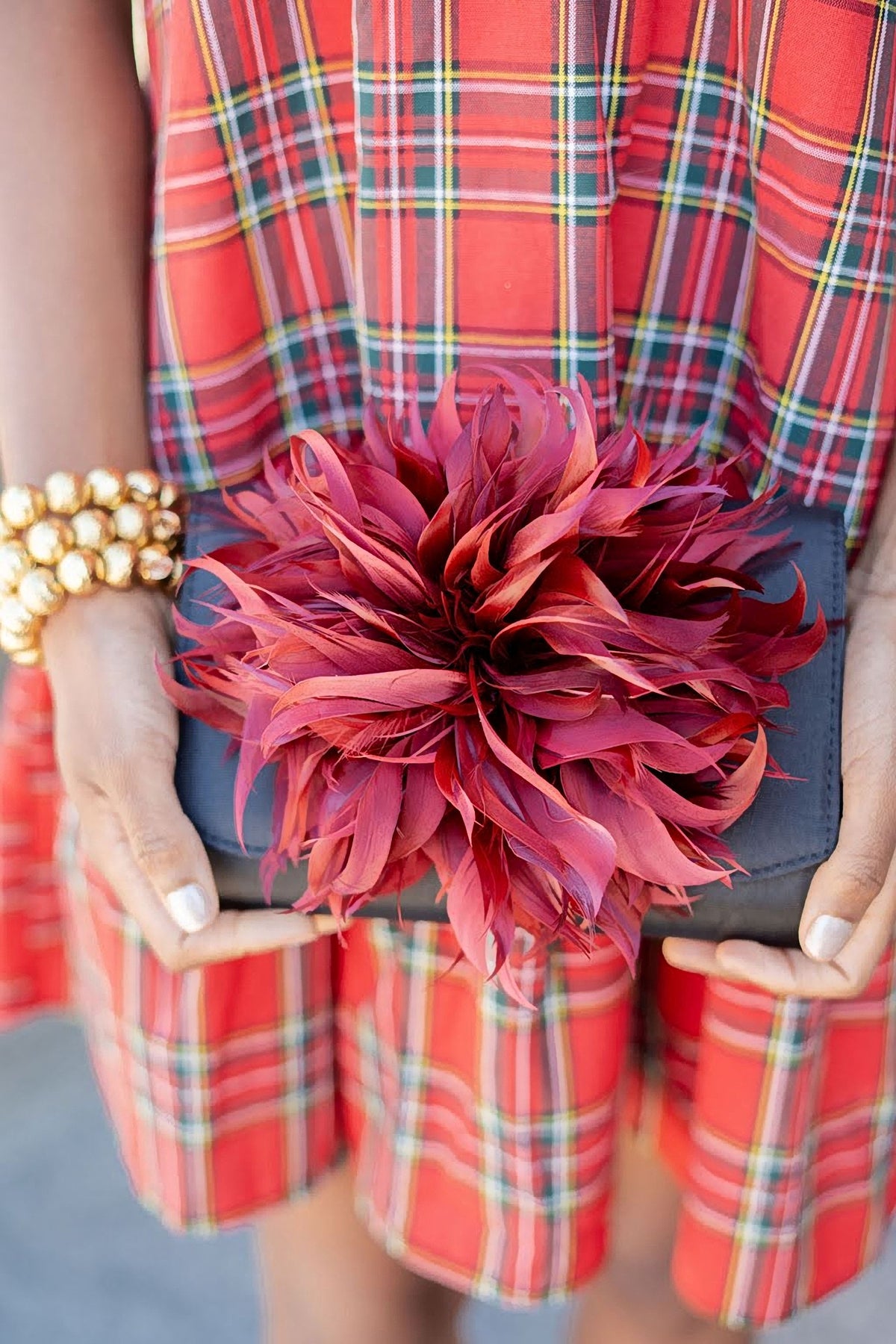 The Black Scallop Ruby Feather Clutch held against a red plaid skirt.