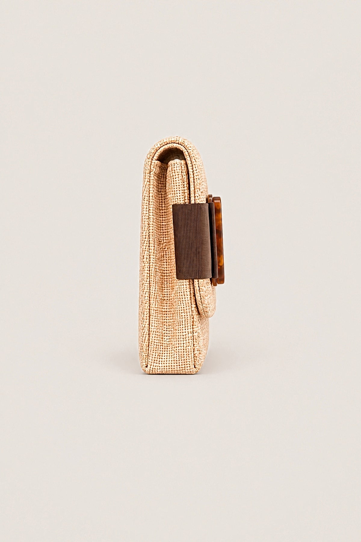 Side view of the Avery straw clutch showing its slim depth and the tortoise buckle.