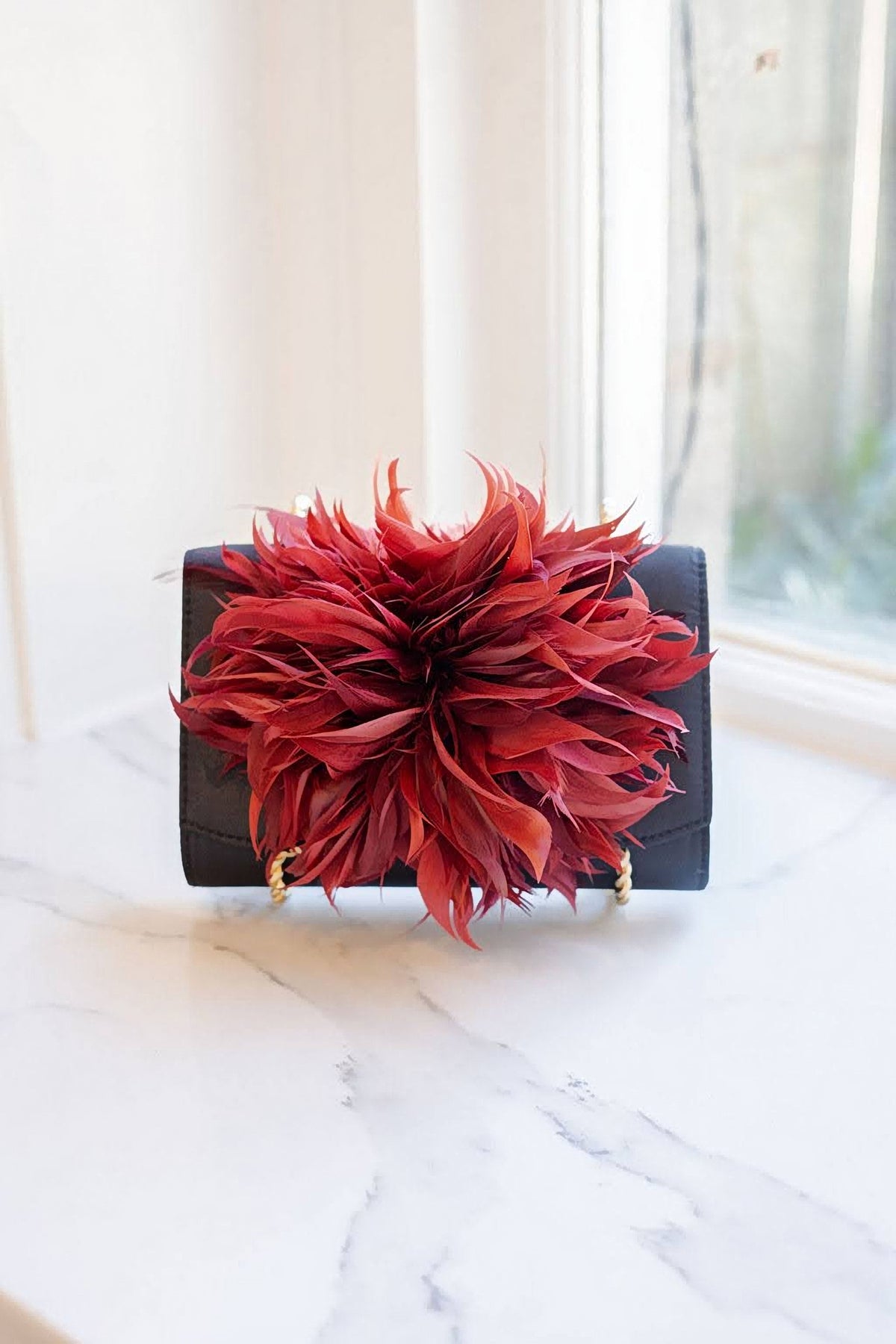 The Black Scallop Ruby Feather Clutch on a marble table by a window.