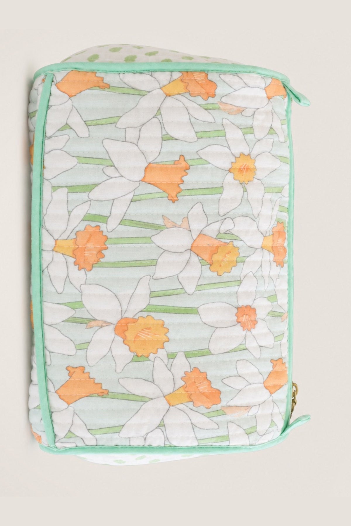 A quilted fabric pouch featuring a daffodil pattern in white, orange, and light green, with mint green piping and a zipper closure.