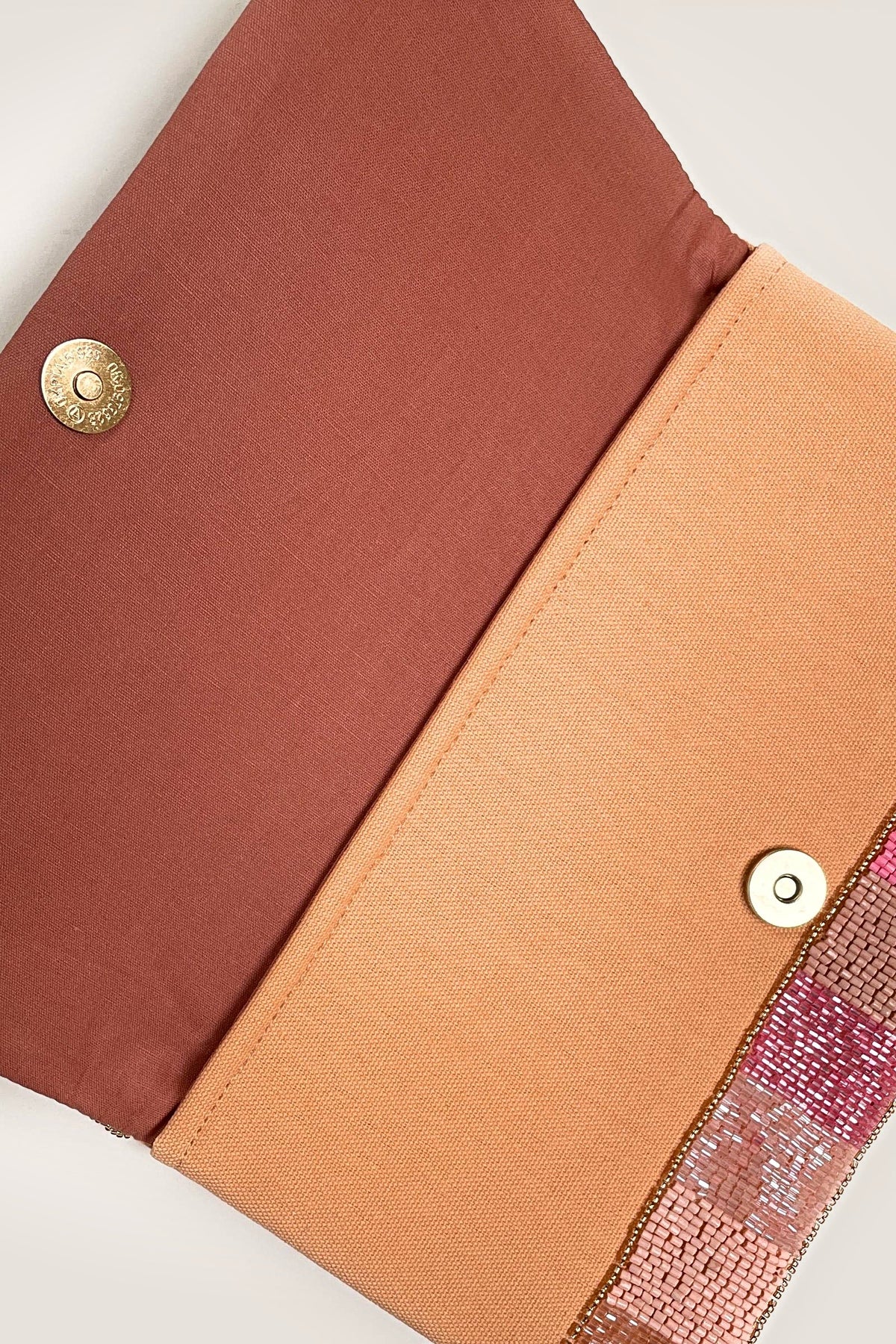 The Rosé All Day Beaded Clutch opened to show its brown flap lining, peach interior and magnetic snap closure.