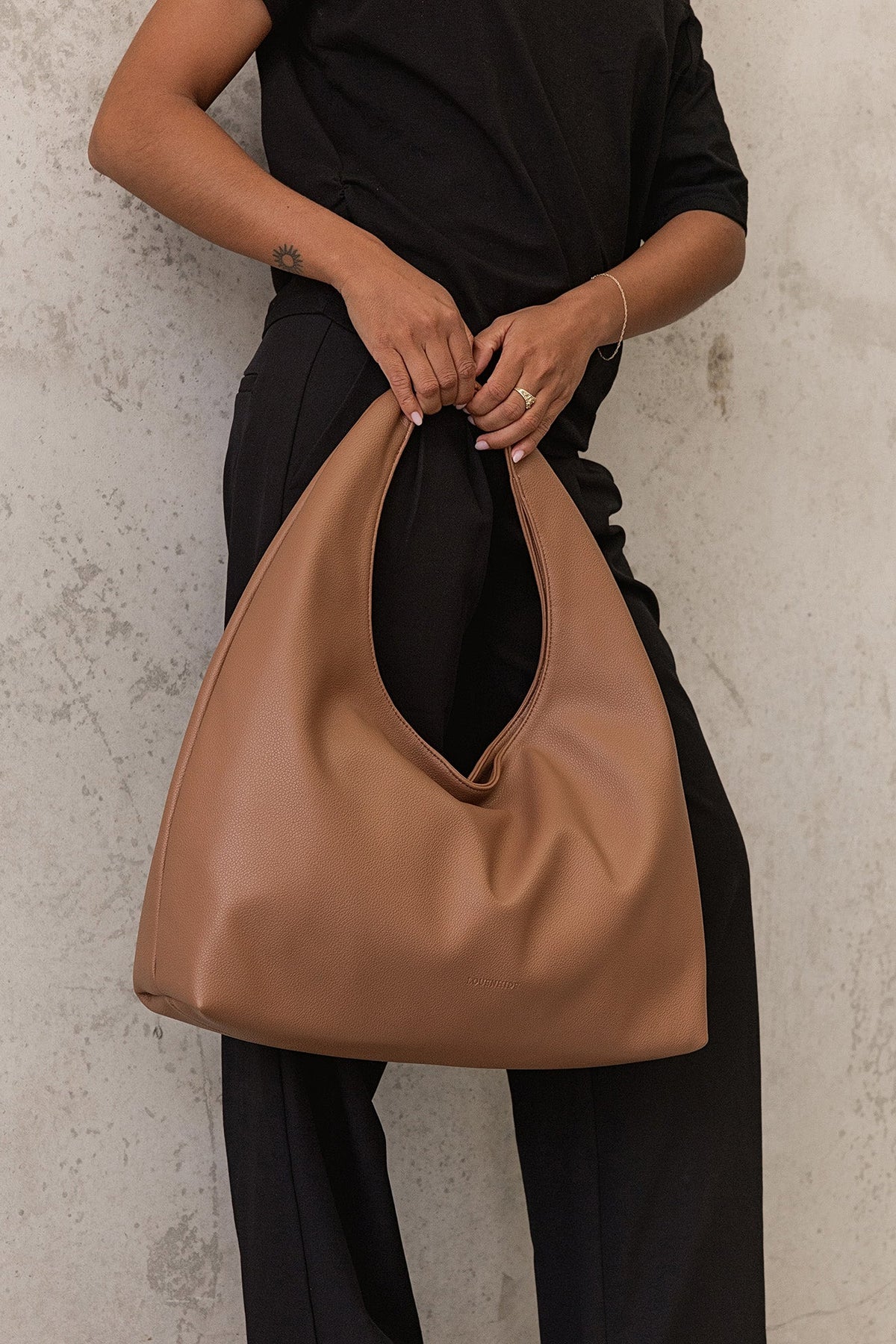 The Monaco Toffee Shoulder Bag held in front with both hands against black trousers and a black top.