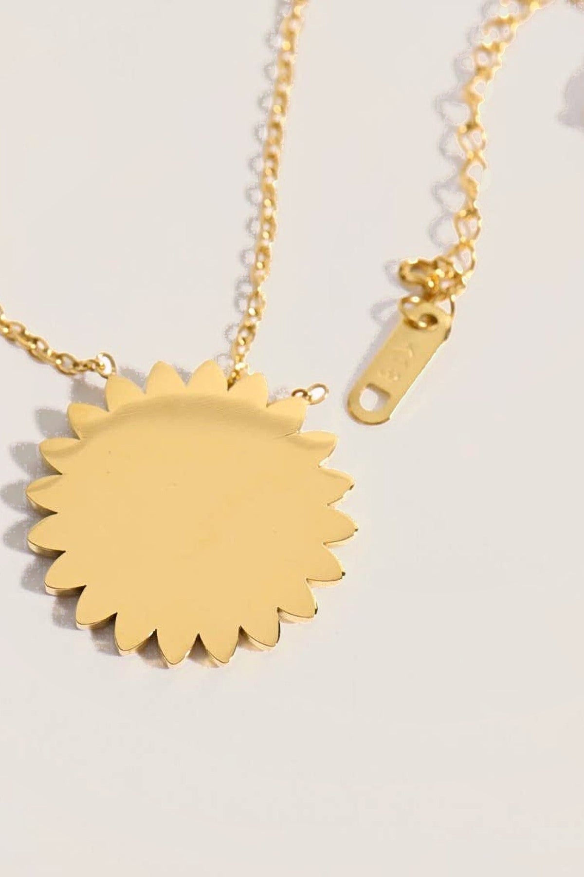 Back of the gold 11:11 Sun Pendant Necklace showing the smooth sunburst pendant, the chain and the extender tag.