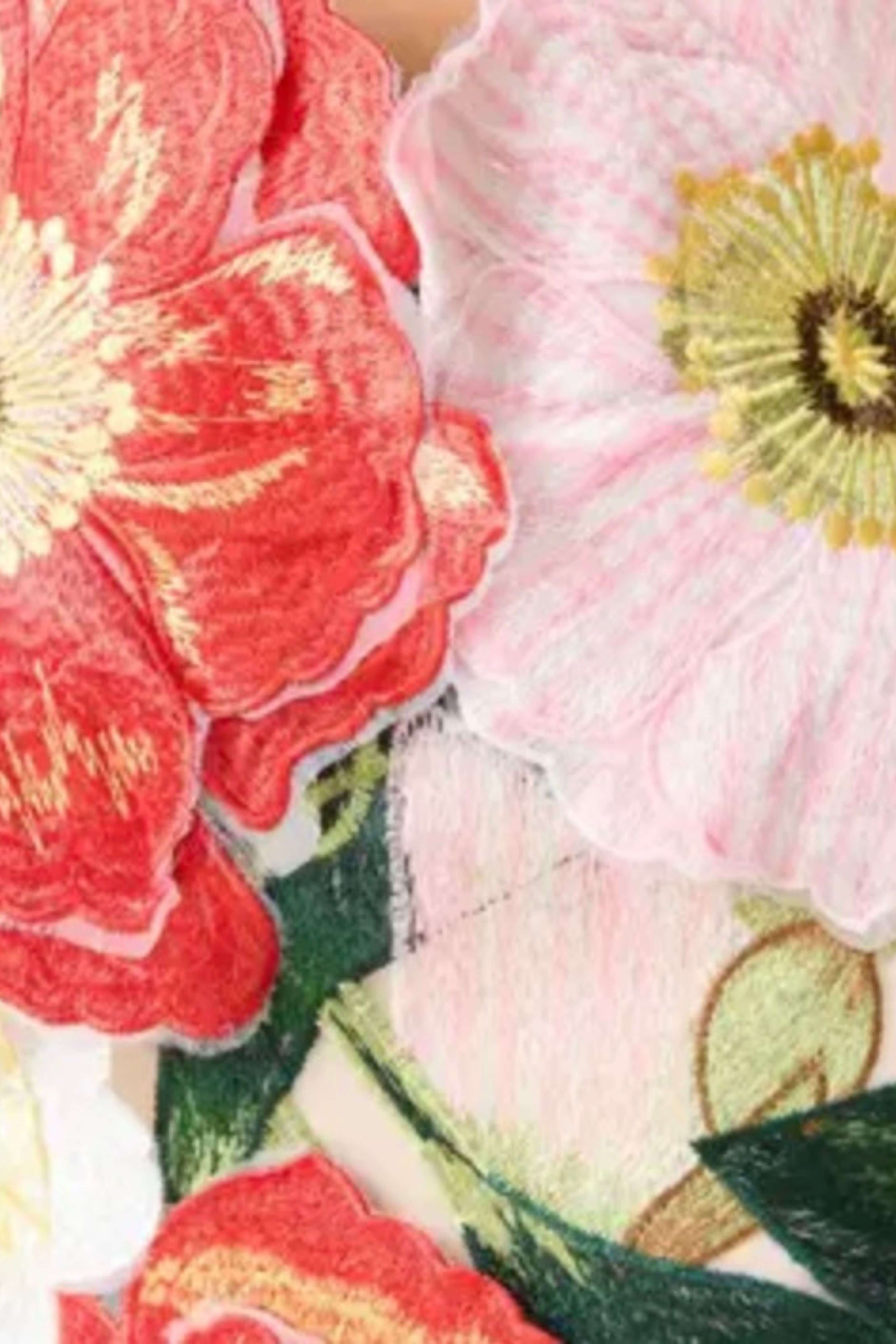 Close-up of embroidered floral patches featuring a large red flower with gold accents, a pale pink flower with a yellow center, and green leaves on a light fabric background.