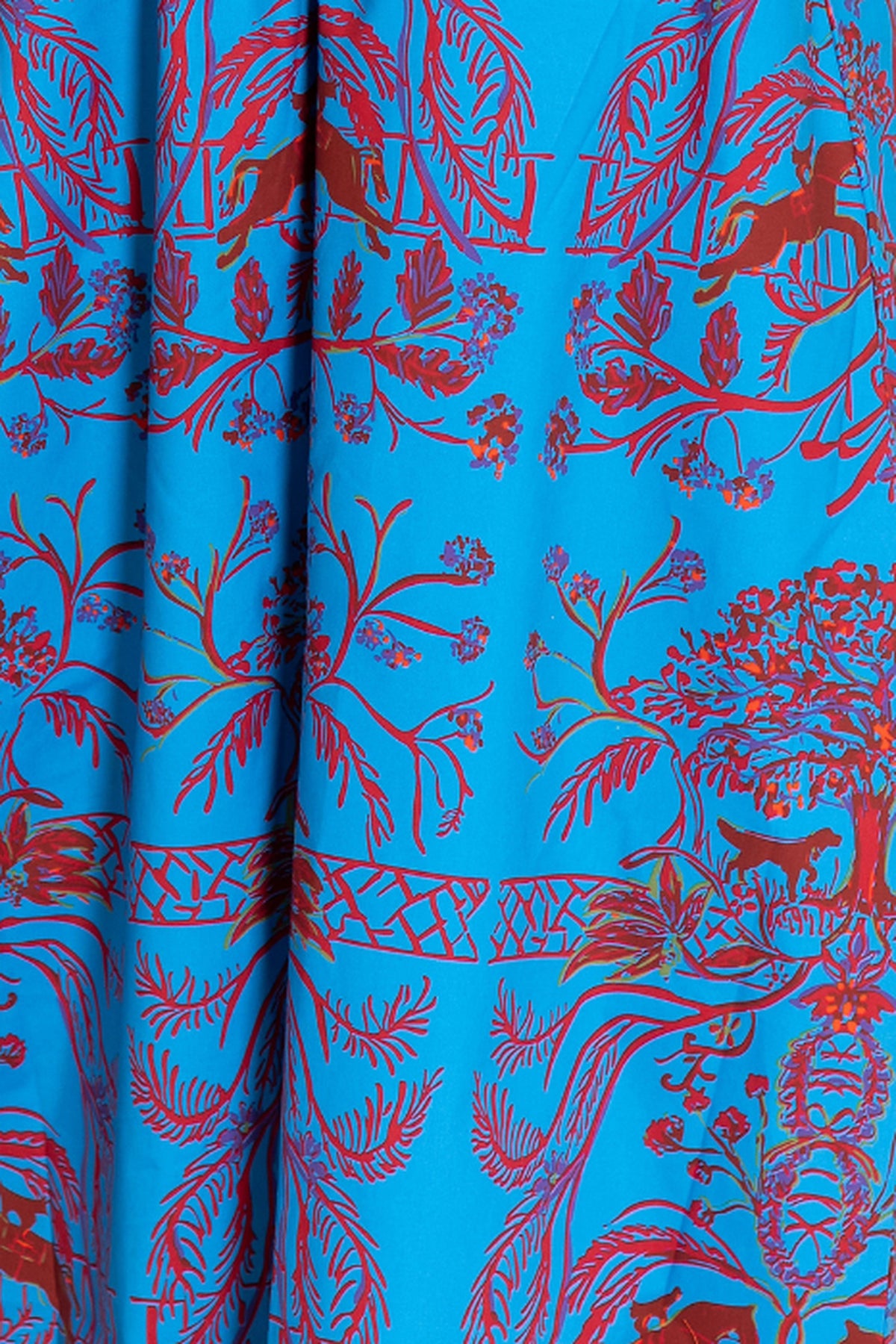 A close-up of a vibrant blue fabric featuring a detailed red and pink botanical and animal print, including trees, birds, and horses.