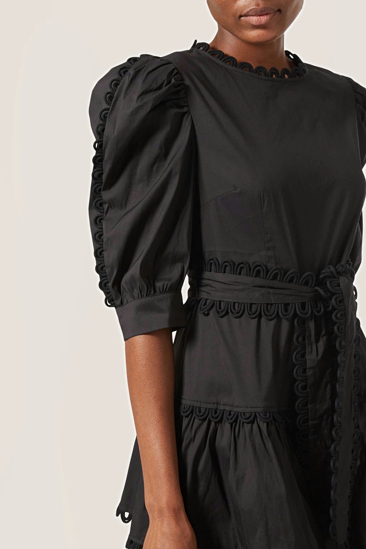 Close-up of the looped trim along the neckline, sleeve seam and tie belt of the black midi dress.
