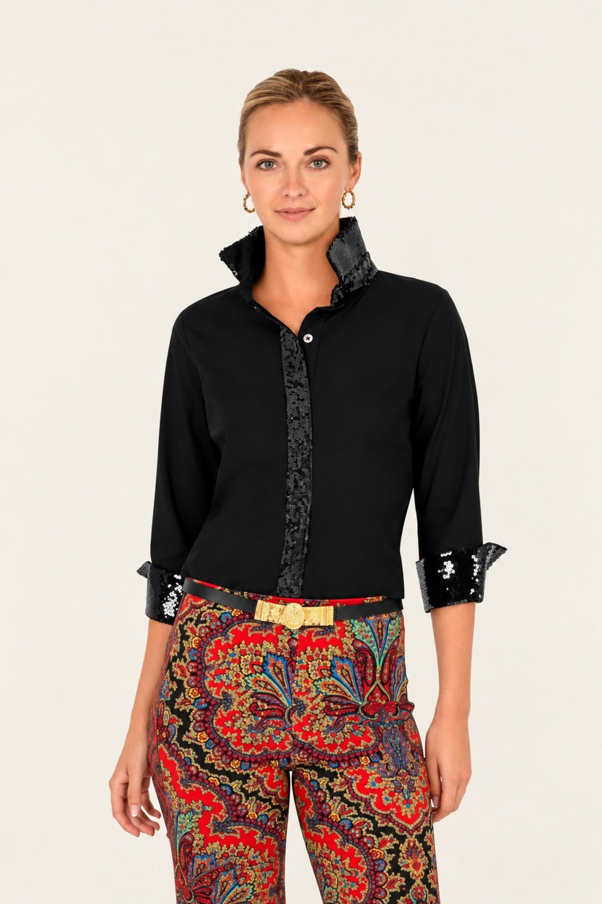 A woman modeling a black long-sleeve button-up shirt with a patterned front placket and black lace-trimmed cuffs, paired with colorful patterned trousers, against a plain light background.