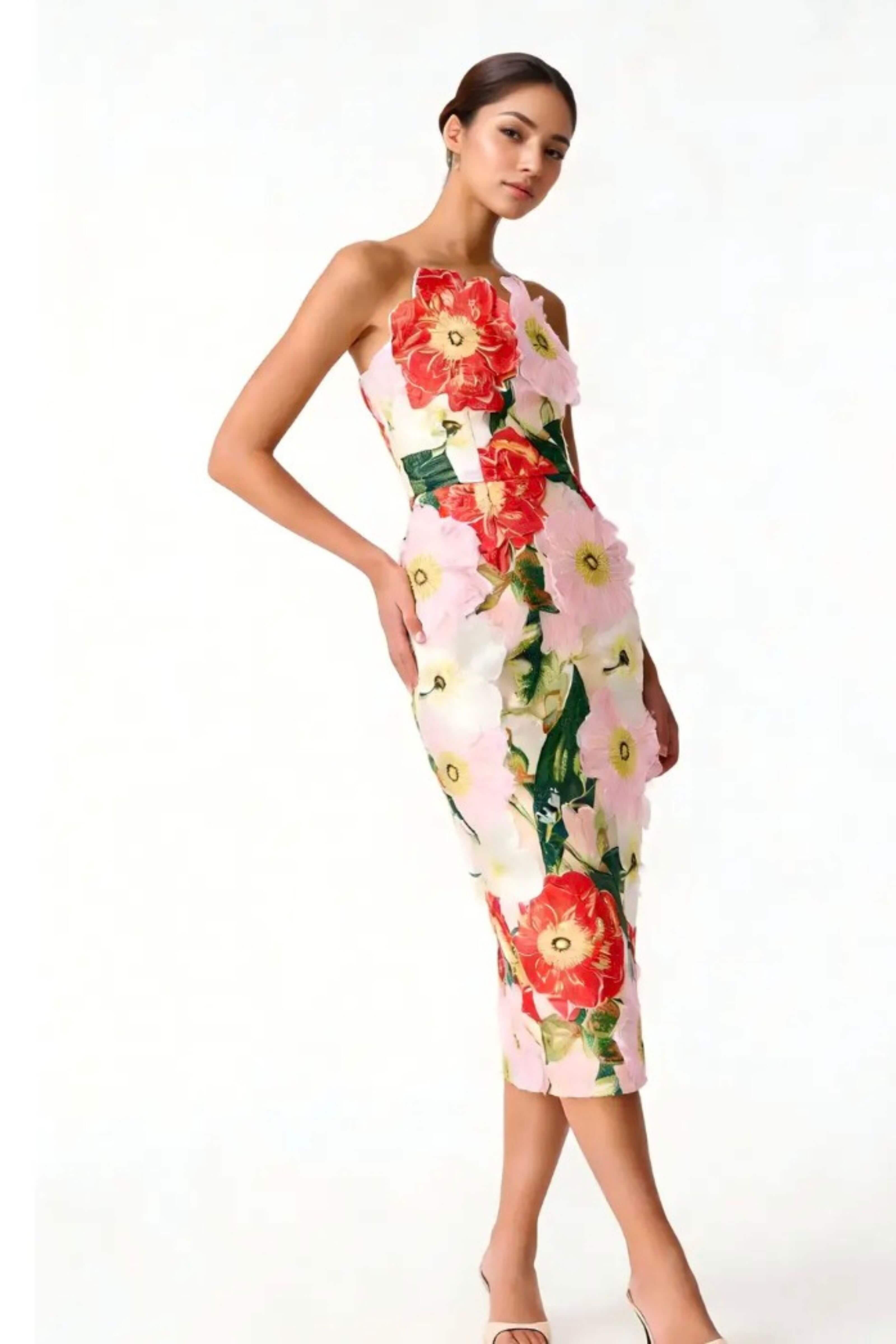 A woman modeling a sleeveless, one-shoulder midi dress with a large floral print in red, pink, and green on a light background, set against a plain white studio backdrop.