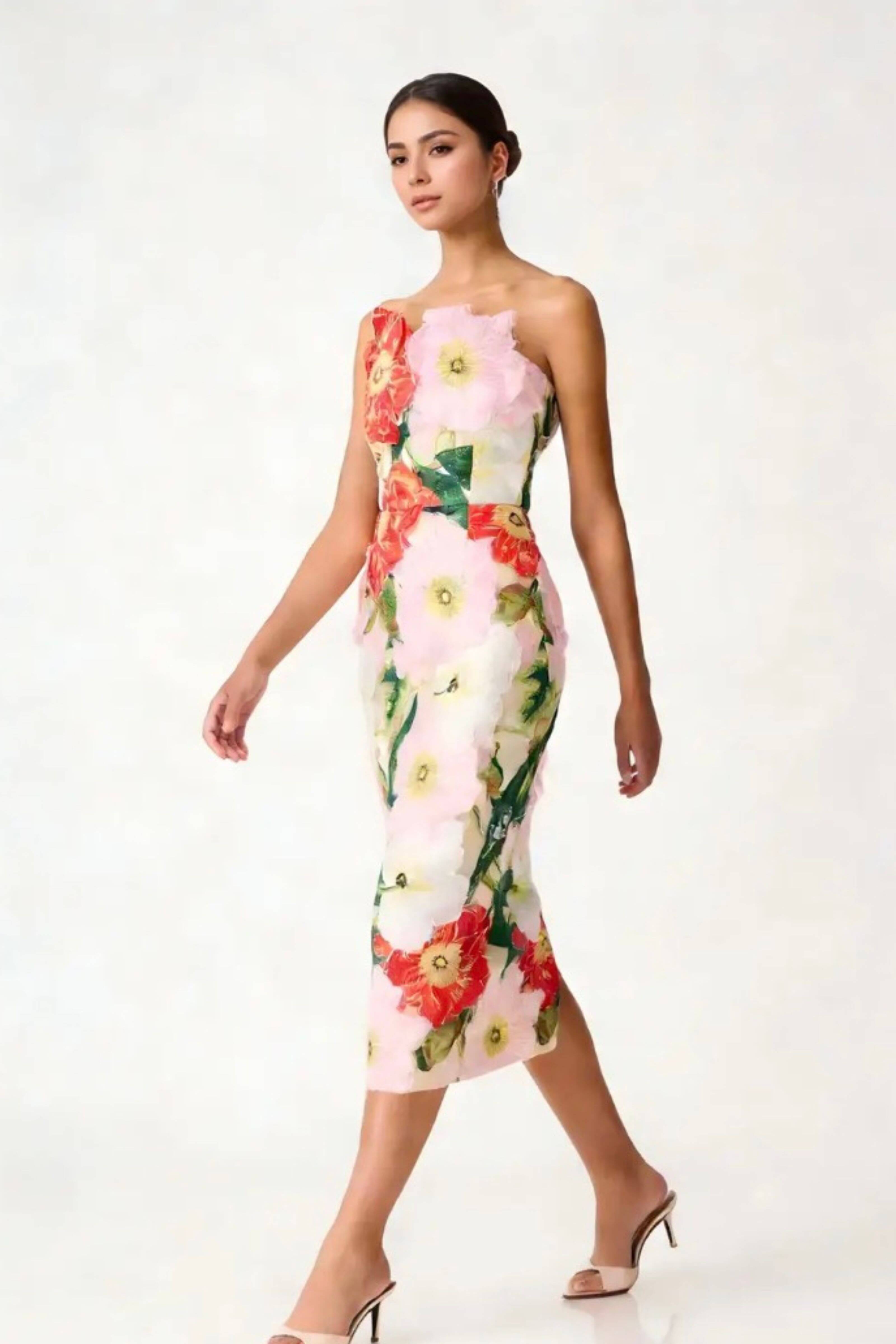 A woman models a strapless midi dress featuring a 3D floral applique pattern in pink, red, and green on a white base, set against a plain white studio background.