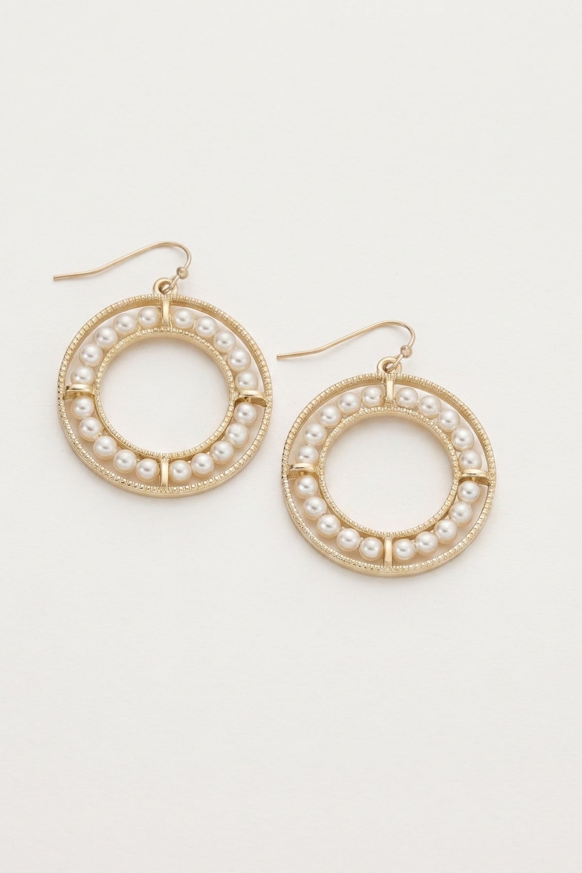 A pair of gold-tone hoop earrings decorated with small white faux pearls, shown on a plain off-white background.