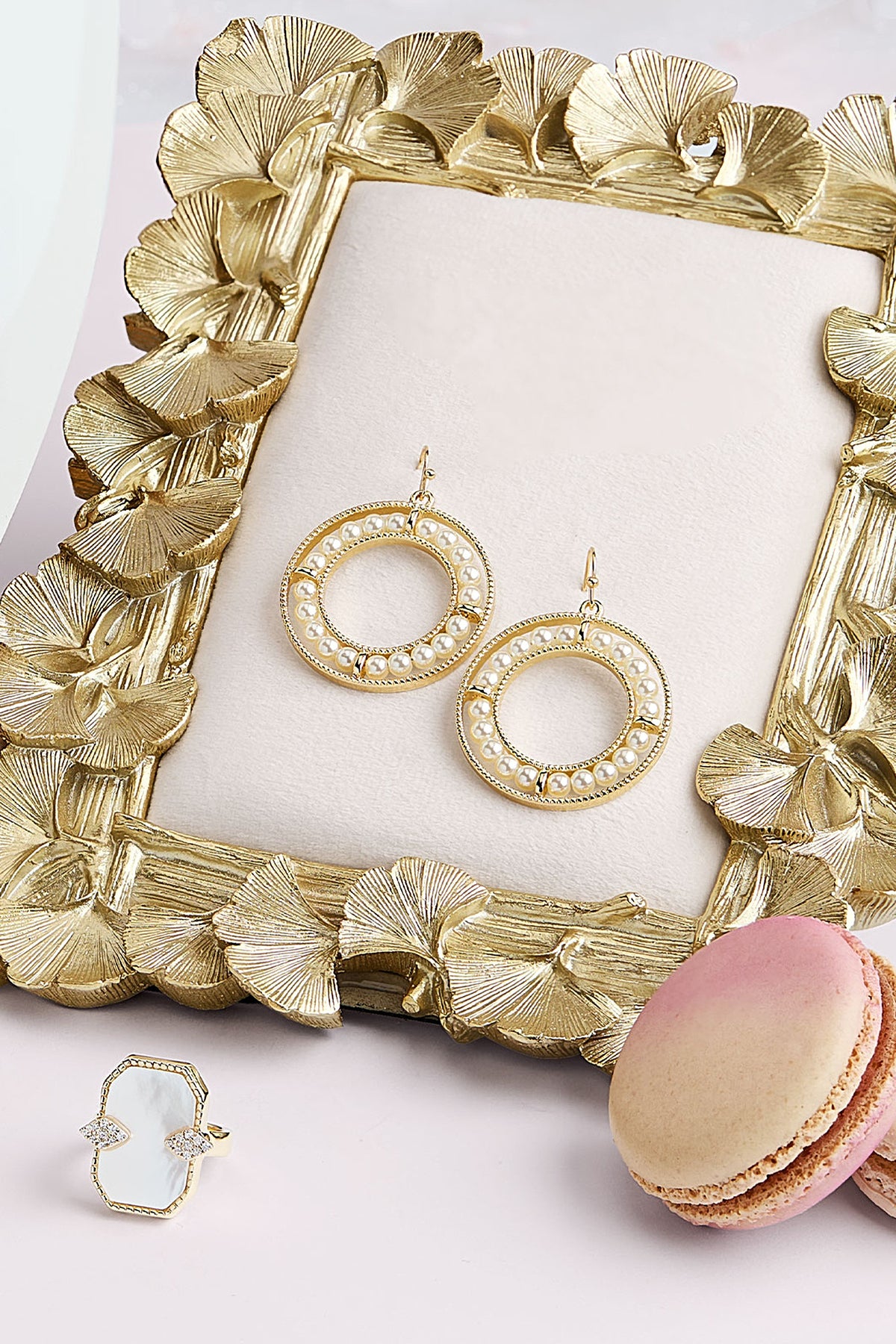 The gold and pearl Coconut drop earrings displayed on a gold ginkgo leaf frame.