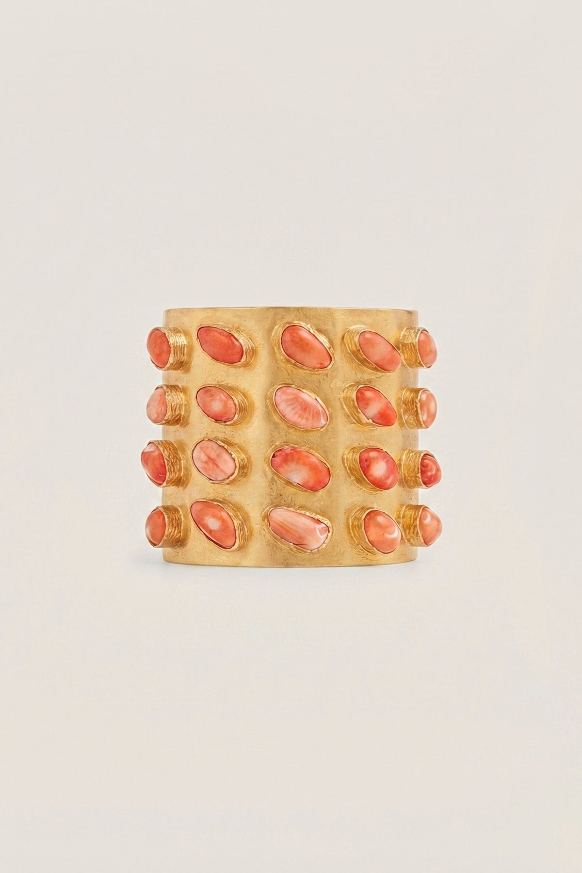 Coral Legacy Cuff, a wide brass cuff set with rows of coral stones, on a warm greige backdrop.