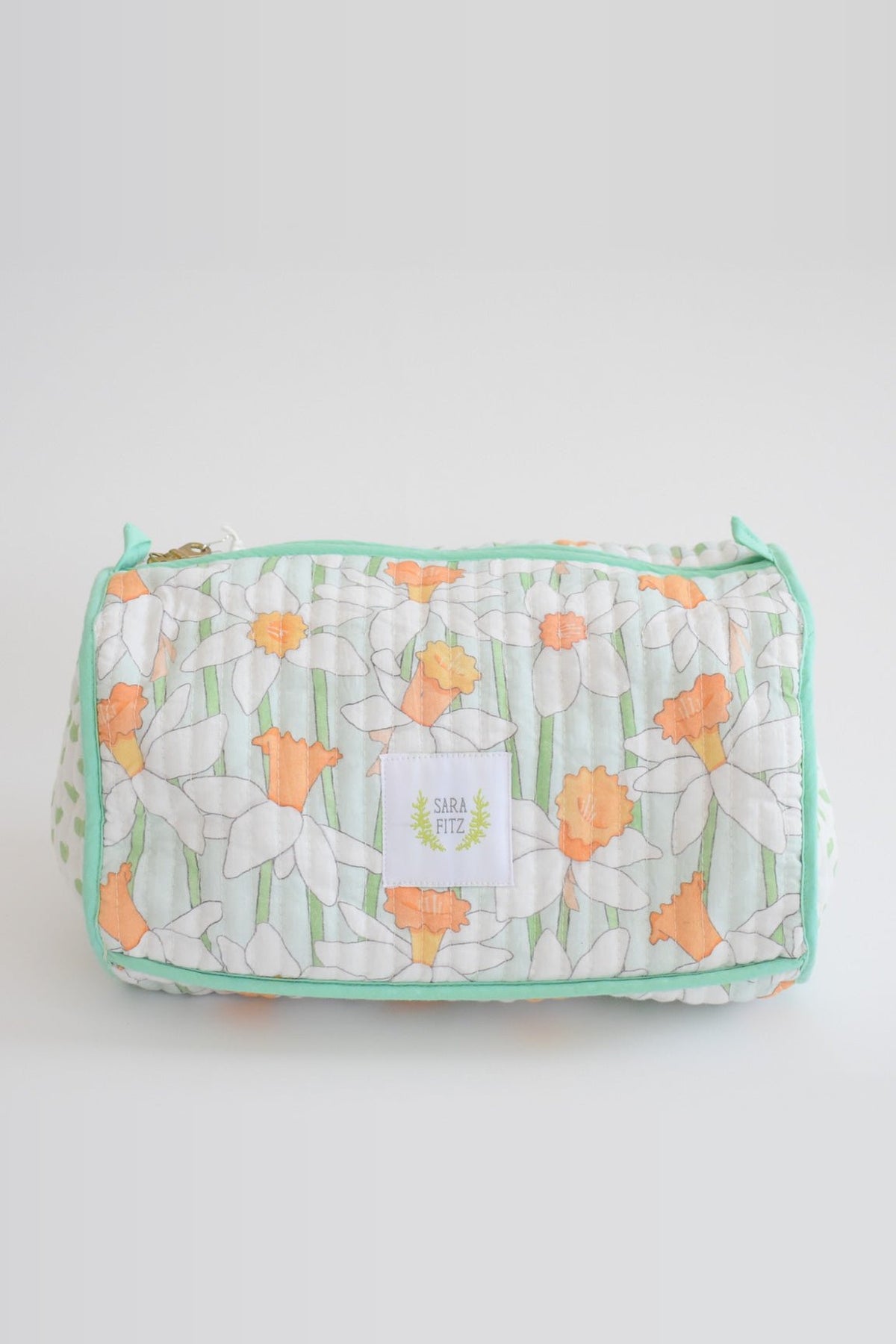 The Daffy quilted cosmetic pouch with white and orange daffodils, mint trim and a Sara Fitz label, shown from the front.
