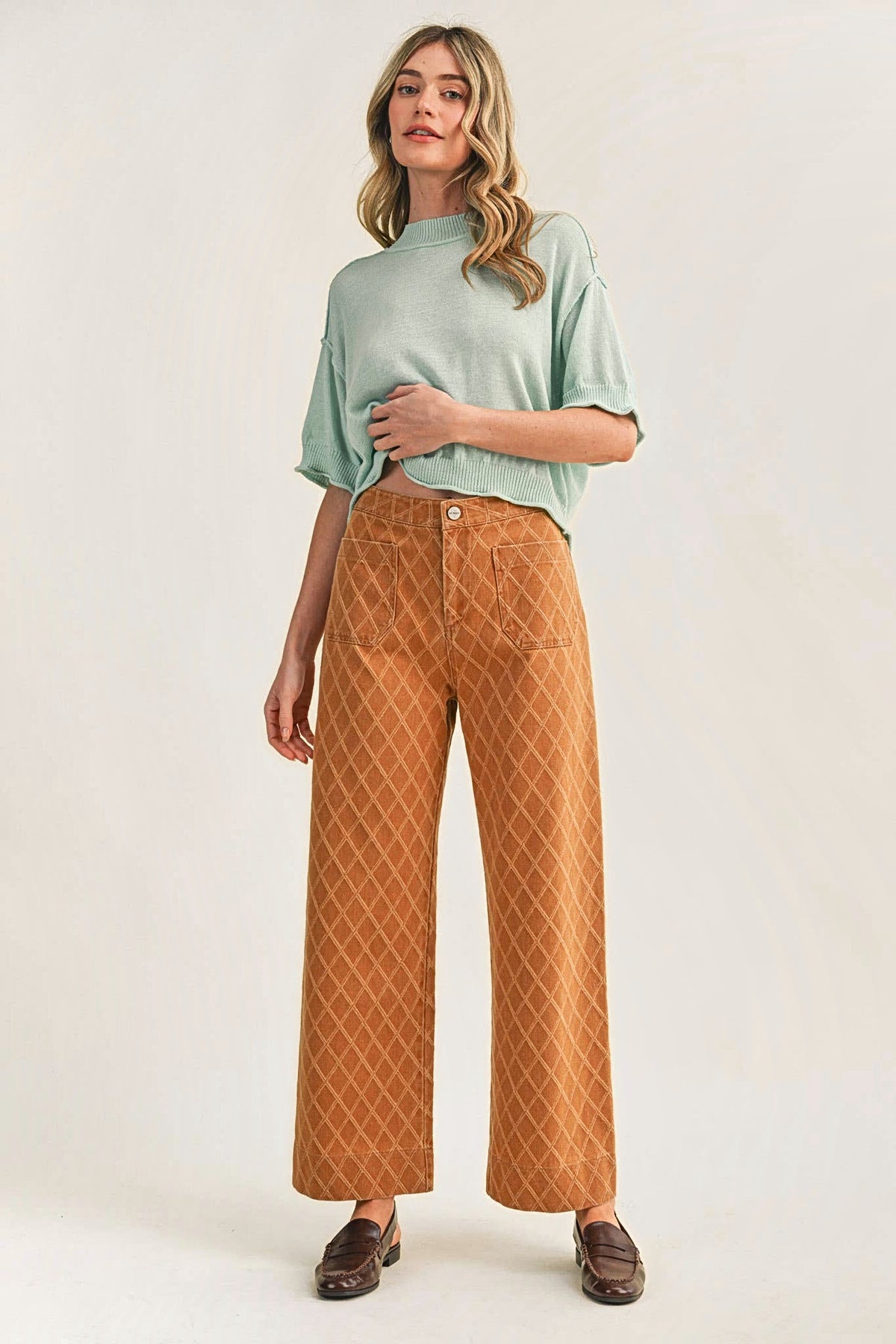 A woman in a mint green knit top and diamond quilted wide-leg pants with brown loafers.