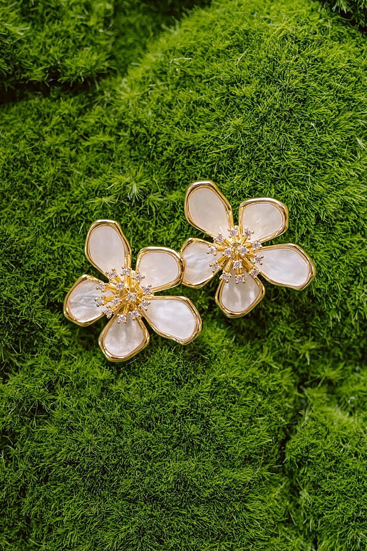 The gold and mother of pearl Elinore flower earrings laid on green moss, showing the petals and crystal centres.