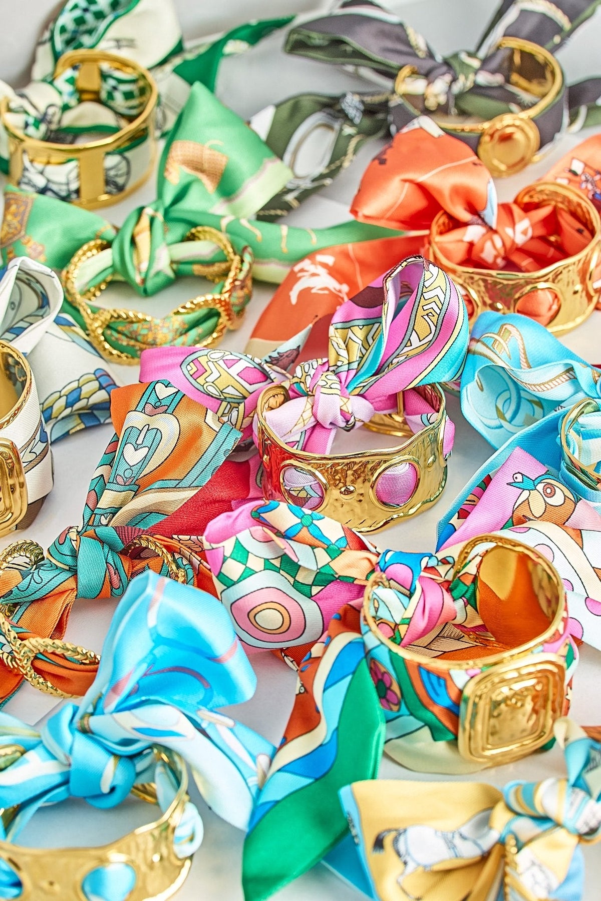 Scarf cuffs tied with silk bows in many prints, showing how the scarf wraps the gold cuff.