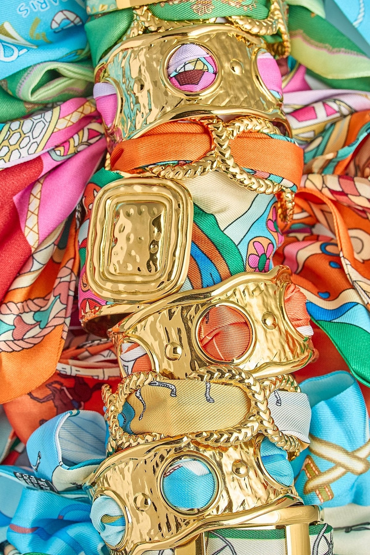 Lisi Lerch gold scarf cuffs, the Evie pink multi among them, stacked on a pile of silk scarves.