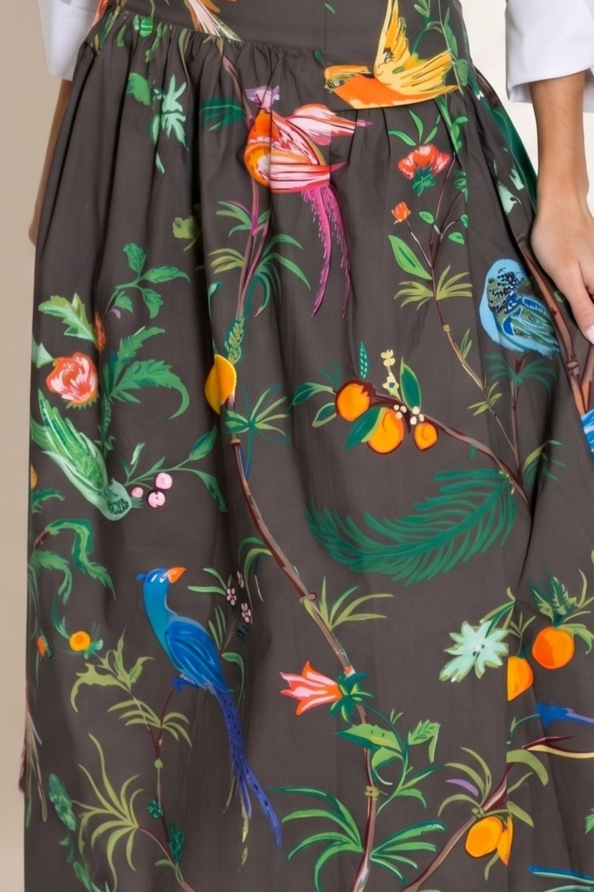 A close-up of a dark brown skirt with a vibrant, multicolored botanical and bird print featuring green leaves, orange fruits, and colorful birds.
